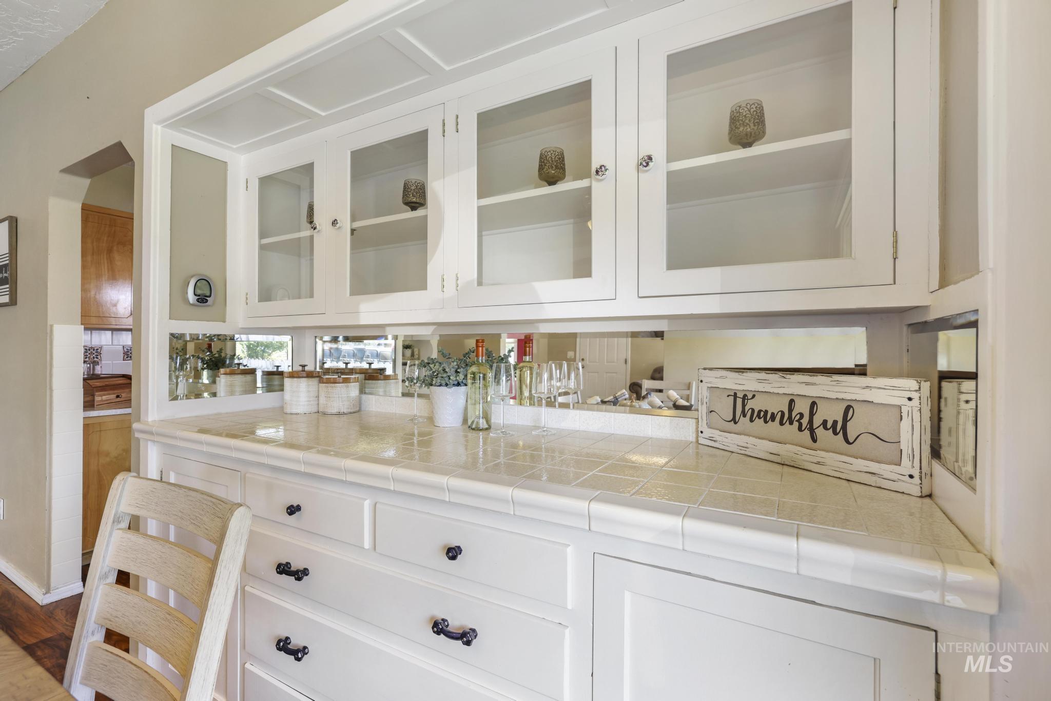 Bar with white cabinets, glass insert cabinets, and tile countertops