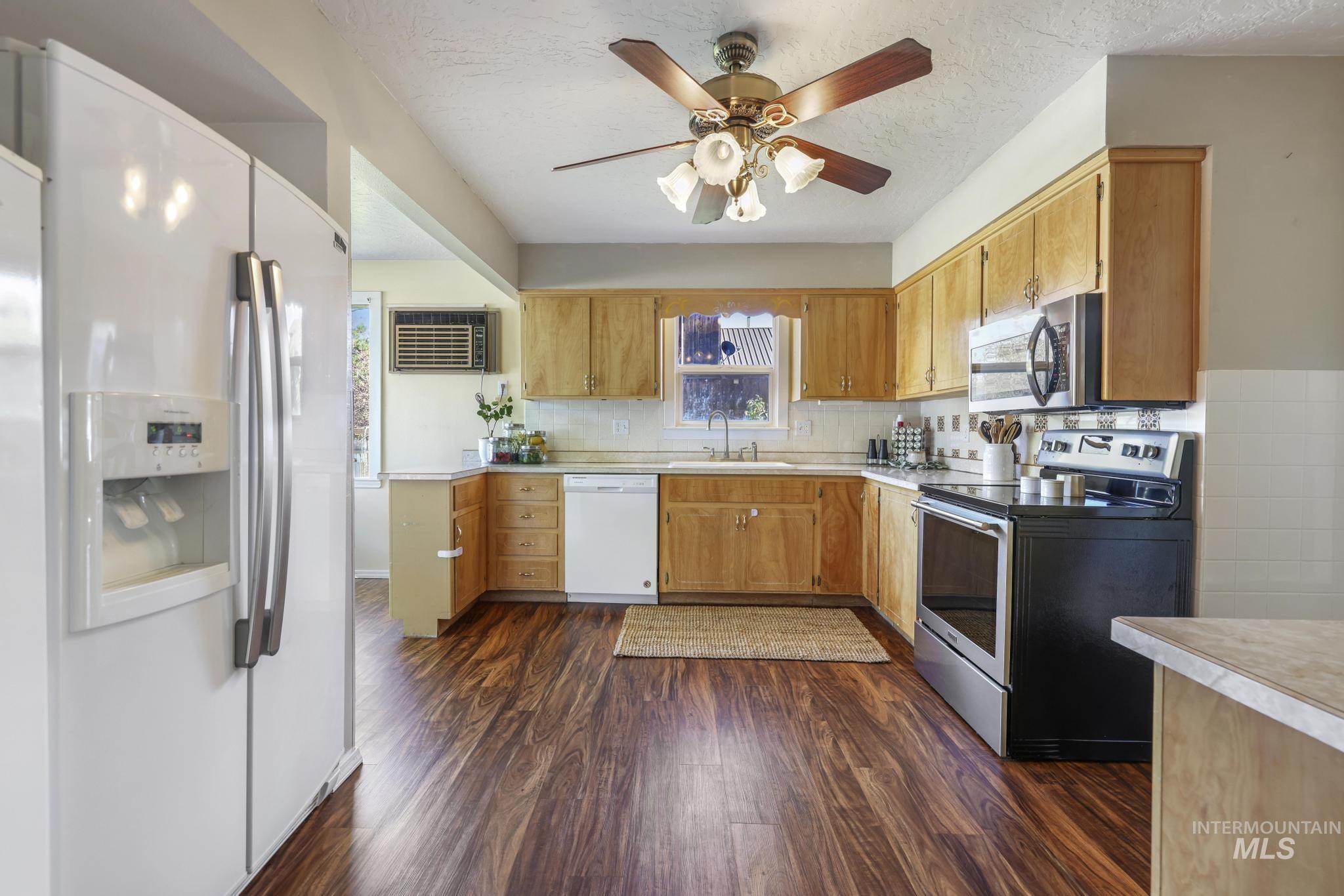 Kitchen with appliances with stainless steel finishes, light countertops, dark wood-style flooring, a ceiling fan, and plenty of natural light