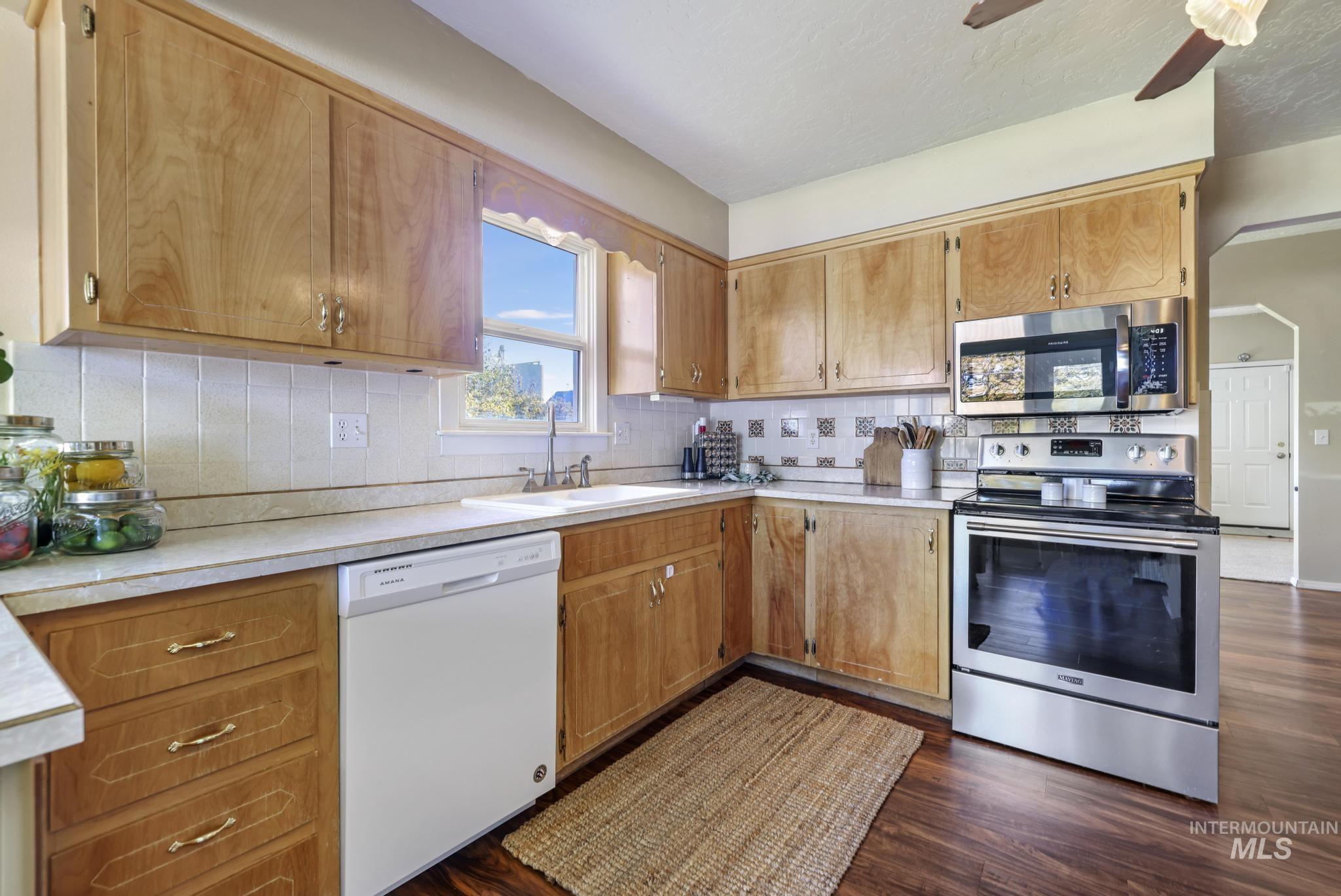 Kitchen featuring appliances with stainless steel finishes, light countertops, dark wood-type flooring, and backsplash