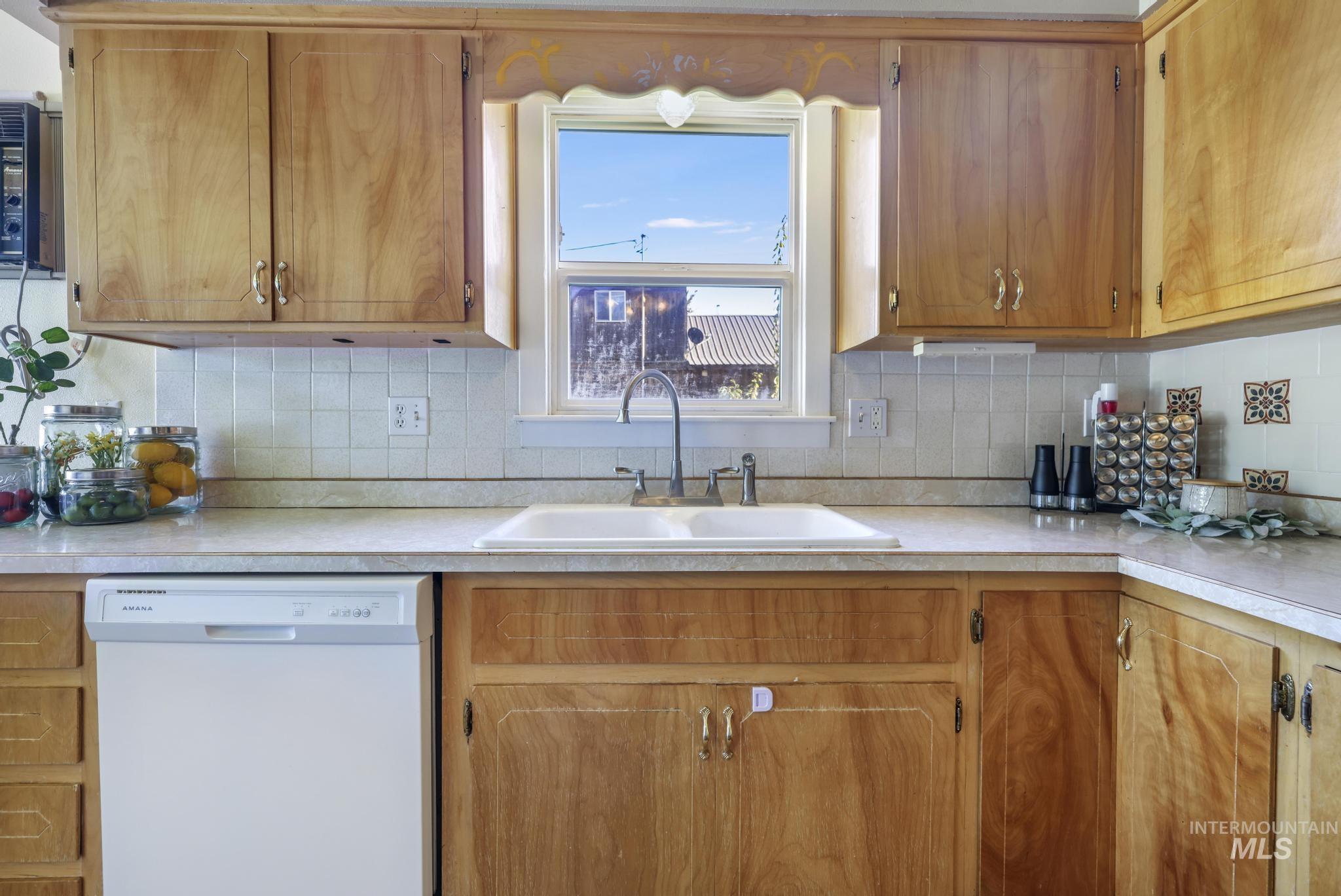 Kitchen featuring light countertops, white dishwasher, tasteful backsplash, and brown cabinets