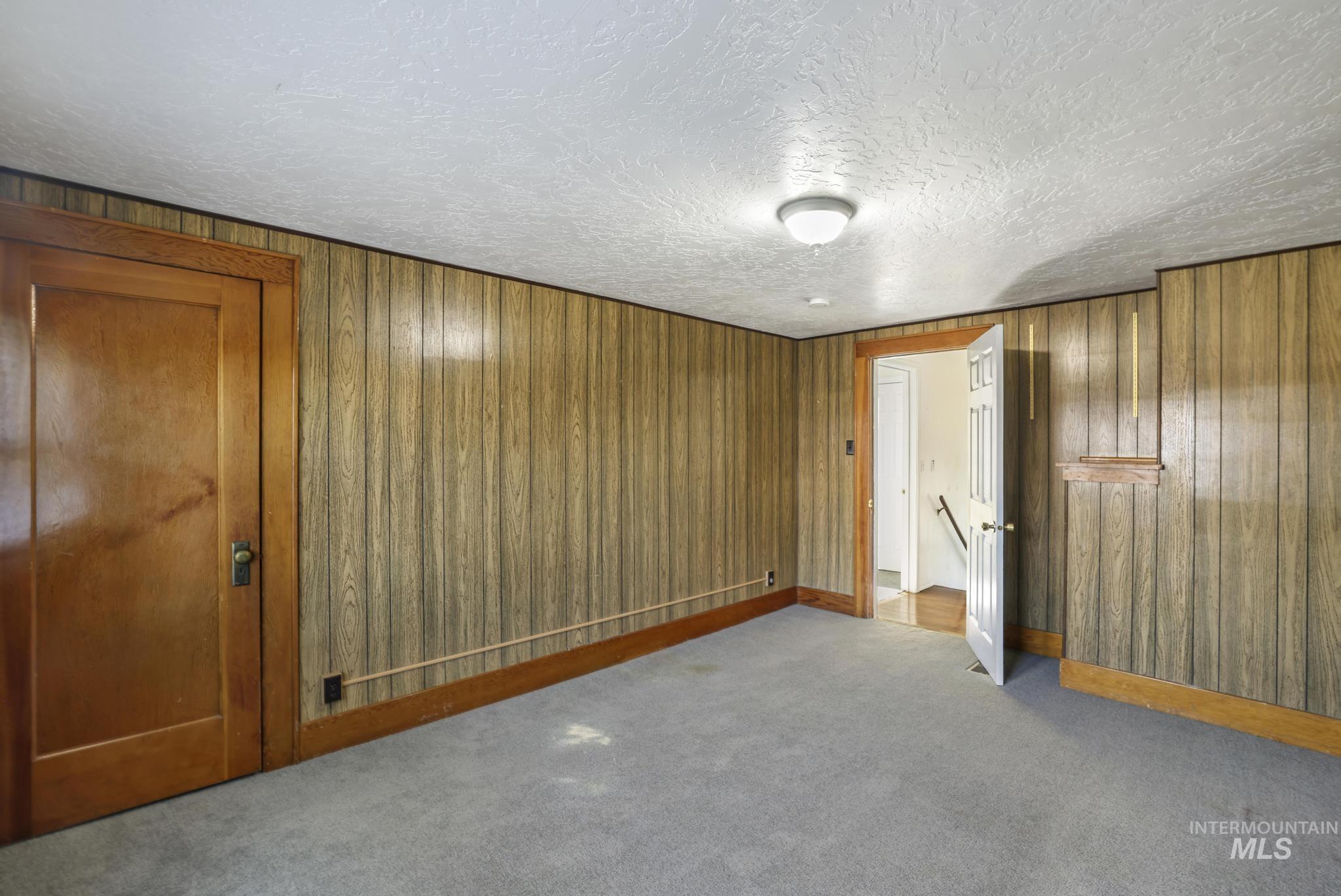 Unfurnished bedroom with carpet floors, wood walls, and a textured ceiling