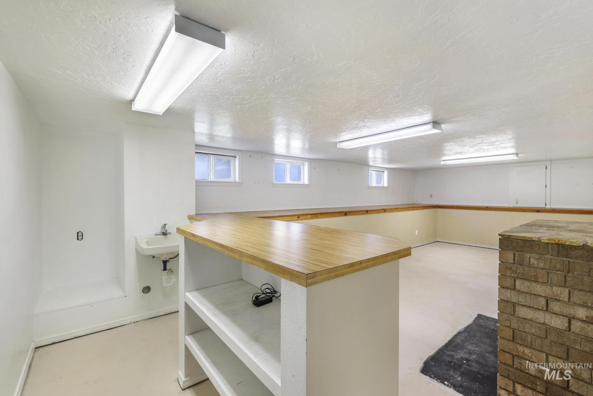Interior space with a textured ceiling, wood counters, concrete floors, open shelves, and a peninsula