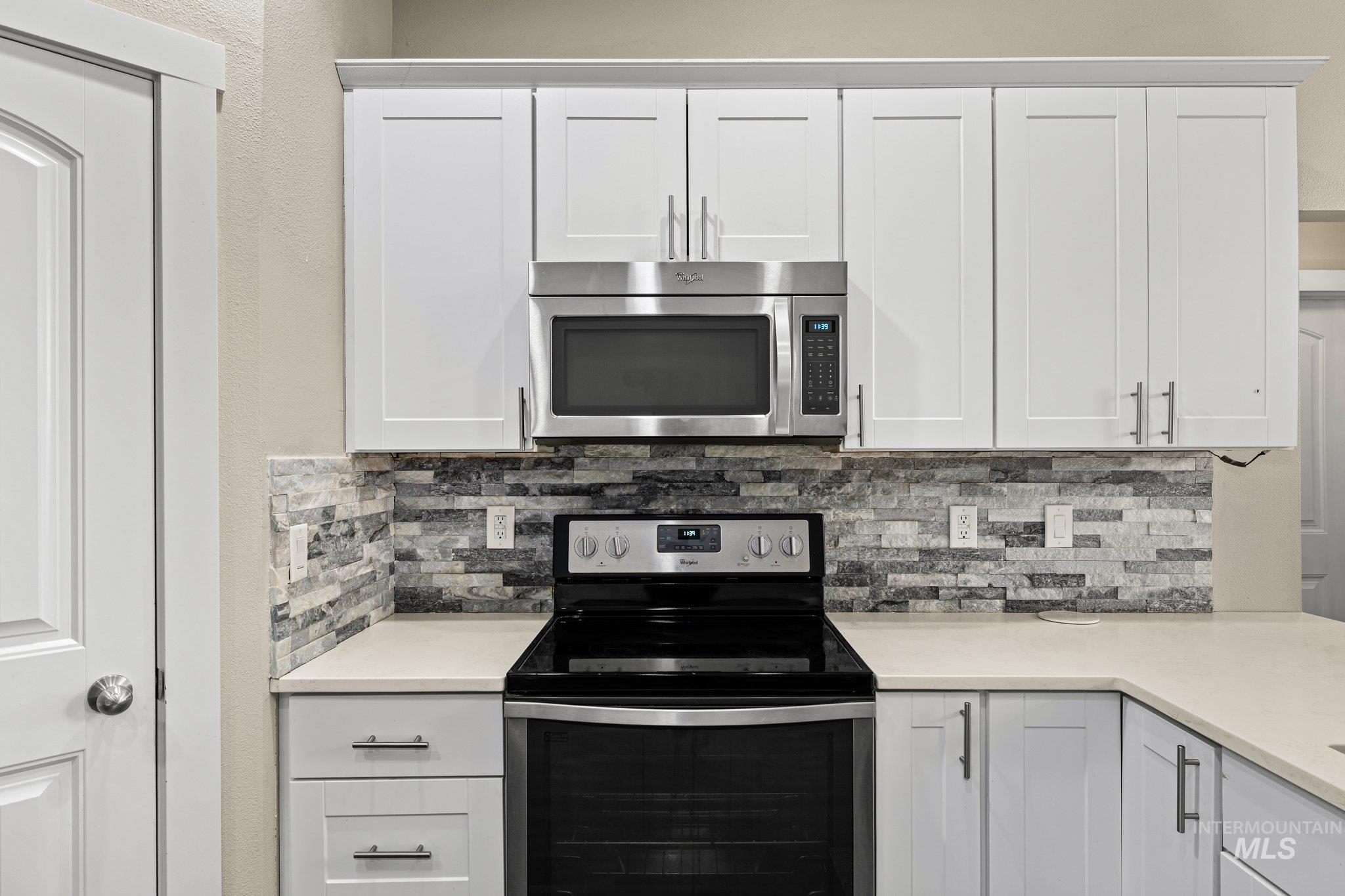 Kitchen with stainless steel appliances, decorative backsplash, and white cabinets