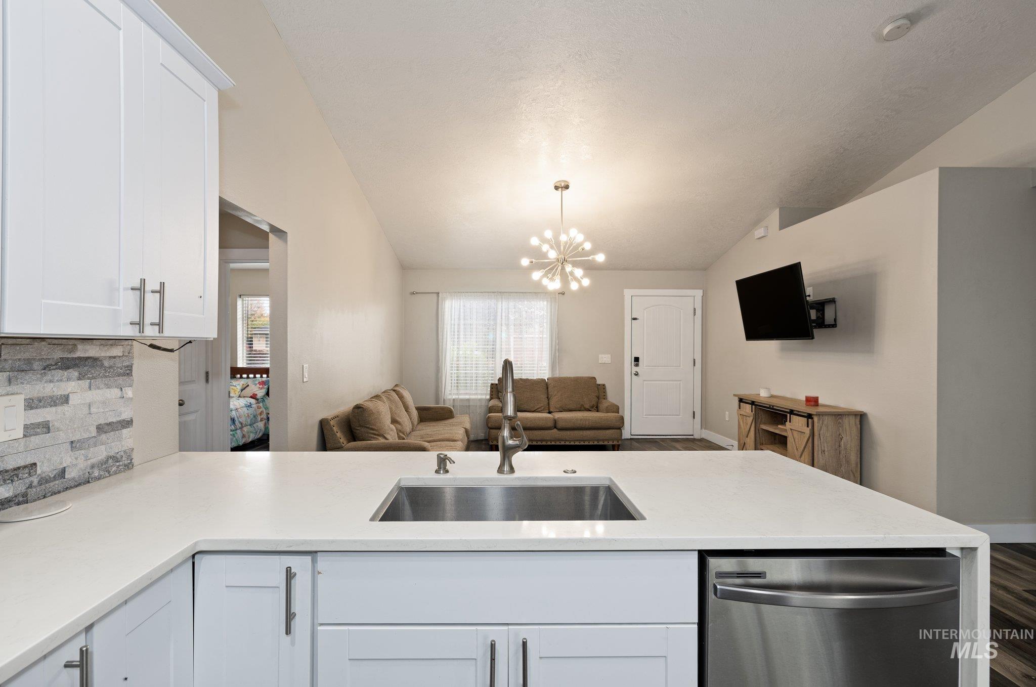 Kitchen featuring open floor plan, tasteful backsplash, stainless steel dishwasher, white cabinetry, and vaulted ceiling