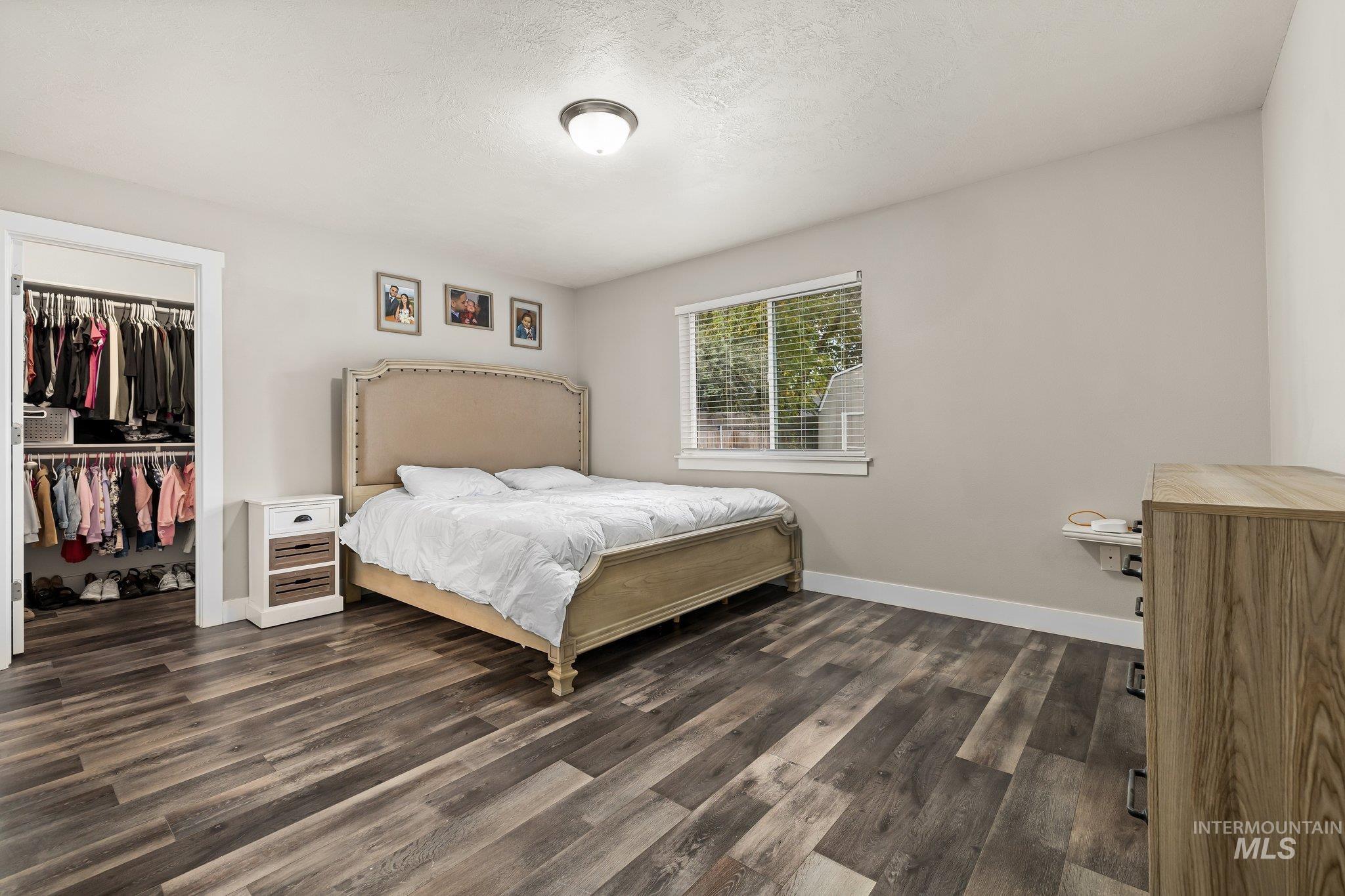 Bedroom featuring dark wood-style floors, a spacious closet, and a textured ceiling