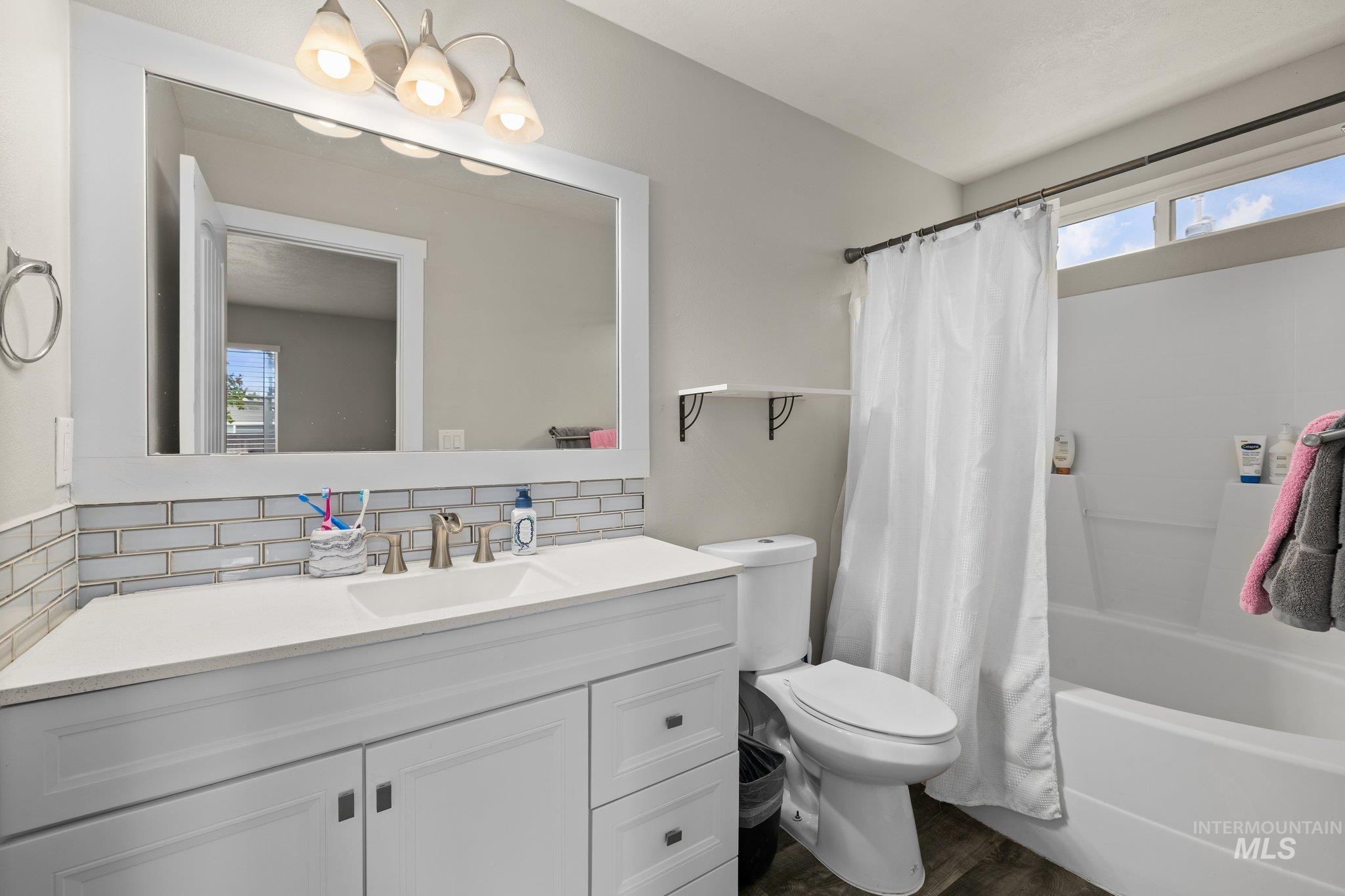 Full bath featuring backsplash, shower / bathtub combination with curtain, vanity, and dark wood-style floors