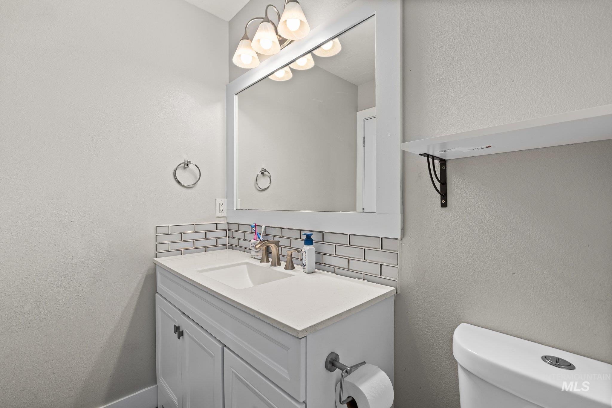 Half bathroom featuring a textured wall, backsplash, and vanity