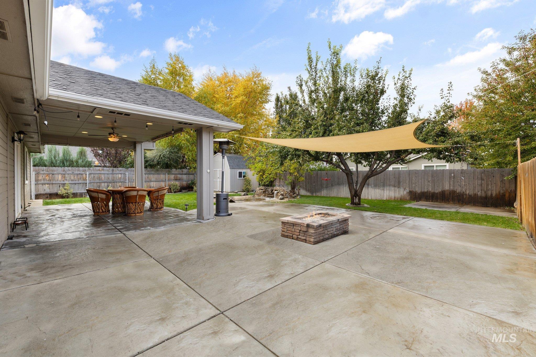 Fenced backyard with a patio, an outdoor fire pit, a storage shed, a ceiling fan, and outdoor dining area