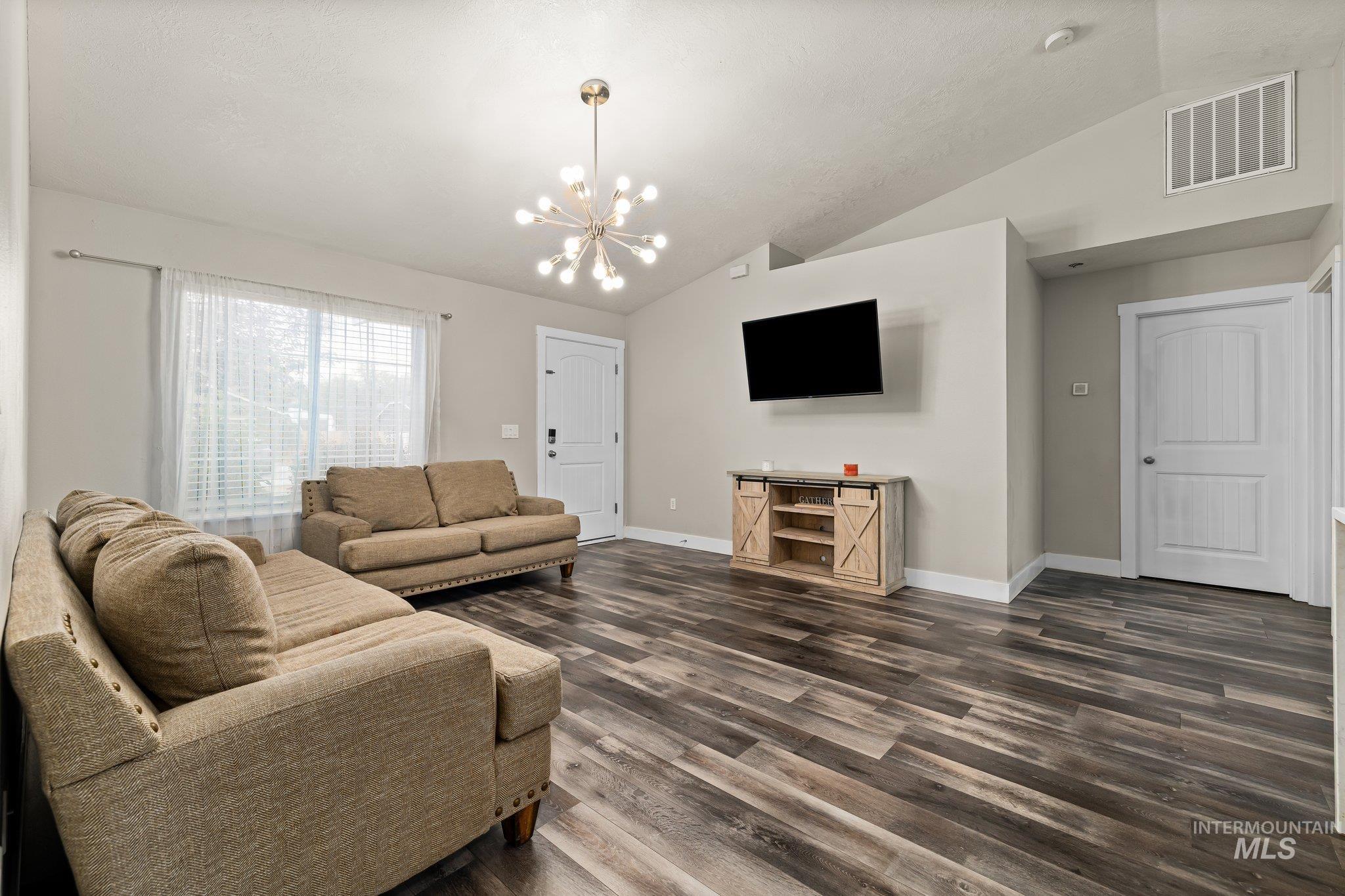 Living room with vaulted ceiling, dark wood-type flooring, and a chandelier