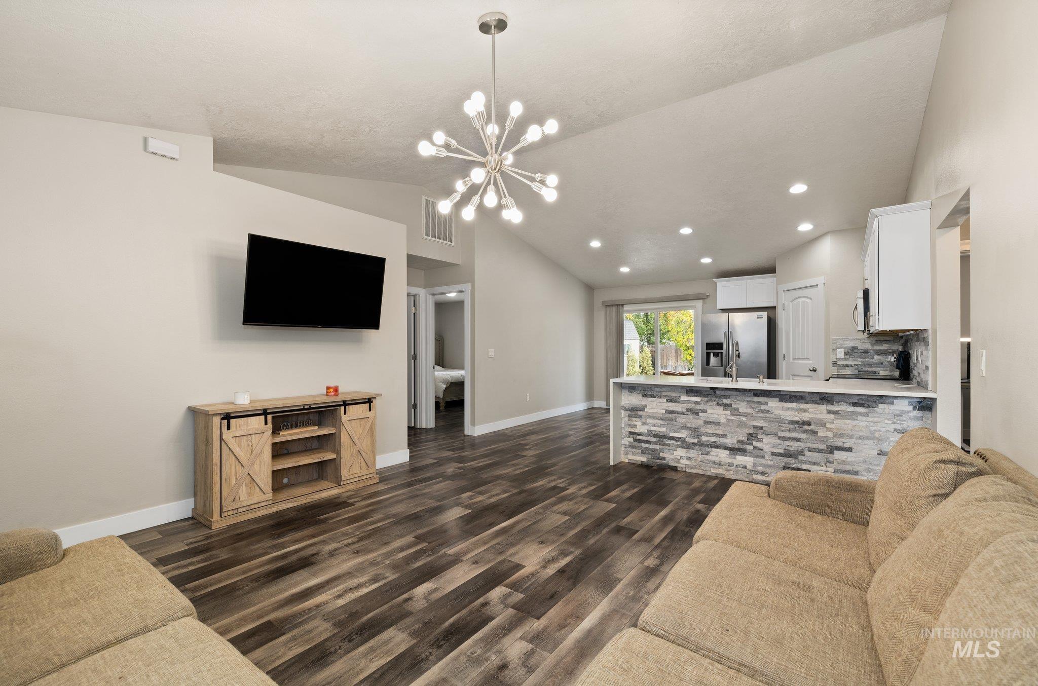 Living area with vaulted ceiling, dark wood-type flooring, a chandelier, and recessed lighting