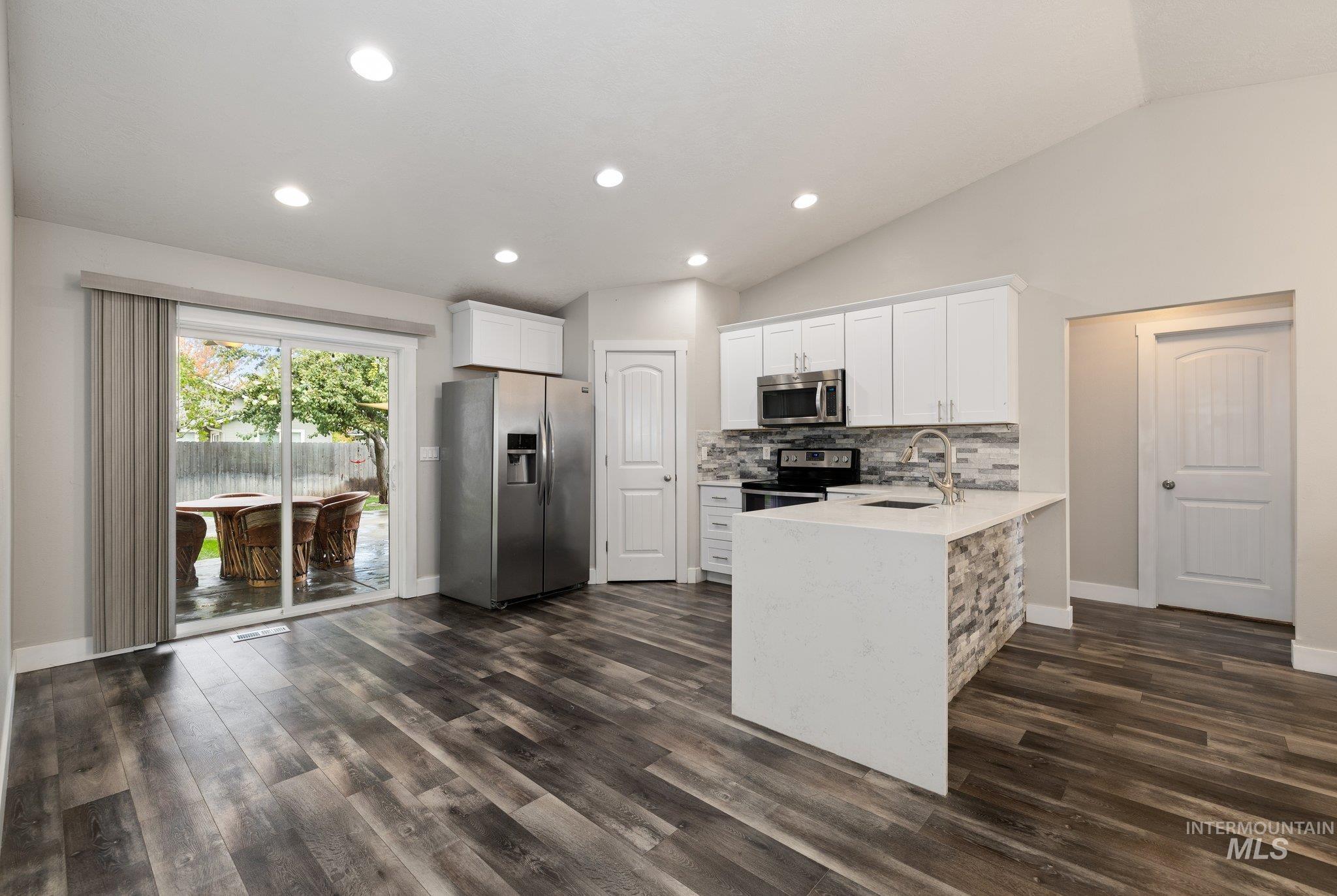 Kitchen with white cabinets, stainless steel appliances, decorative backsplash, a peninsula, and light stone counters