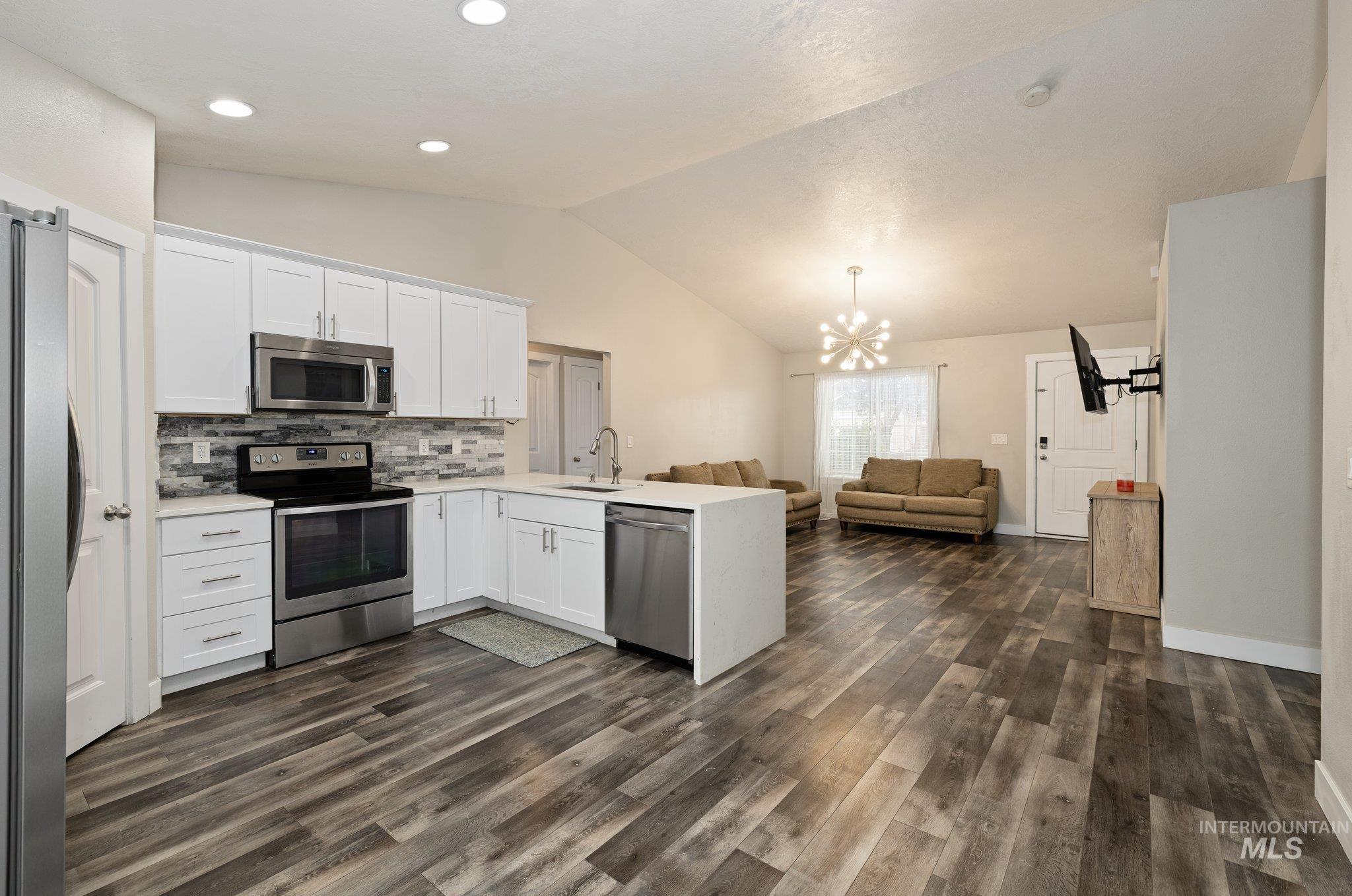 Kitchen with stainless steel appliances, white cabinetry, a peninsula, vaulted ceiling, and open floor plan