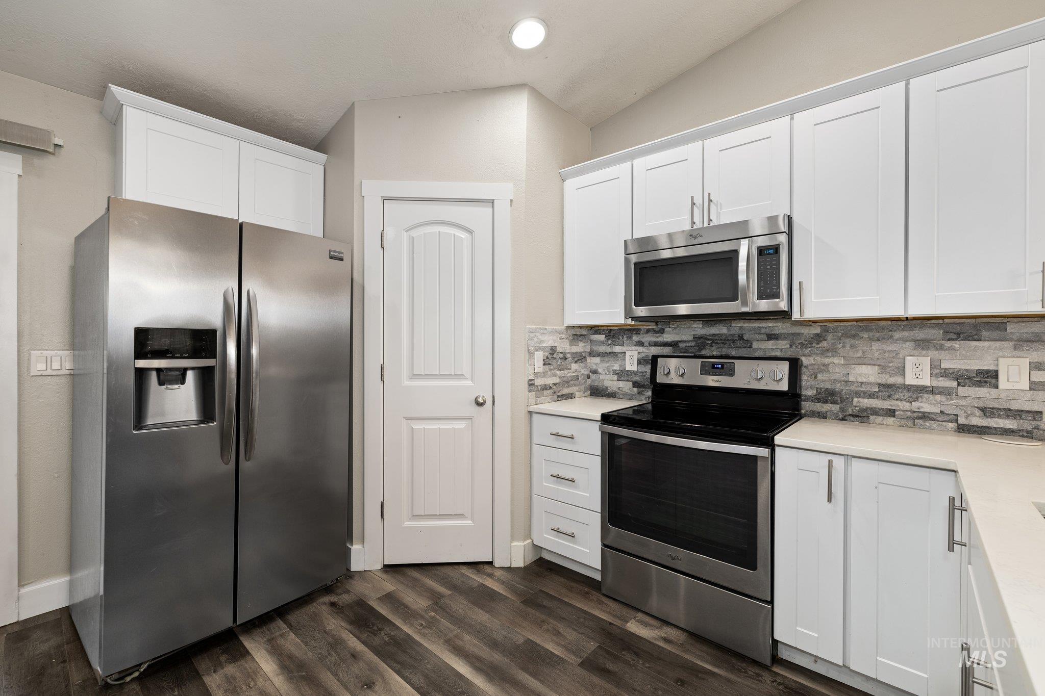 Kitchen with appliances with stainless steel finishes, white cabinetry, dark wood finished floors, backsplash, and recessed lighting