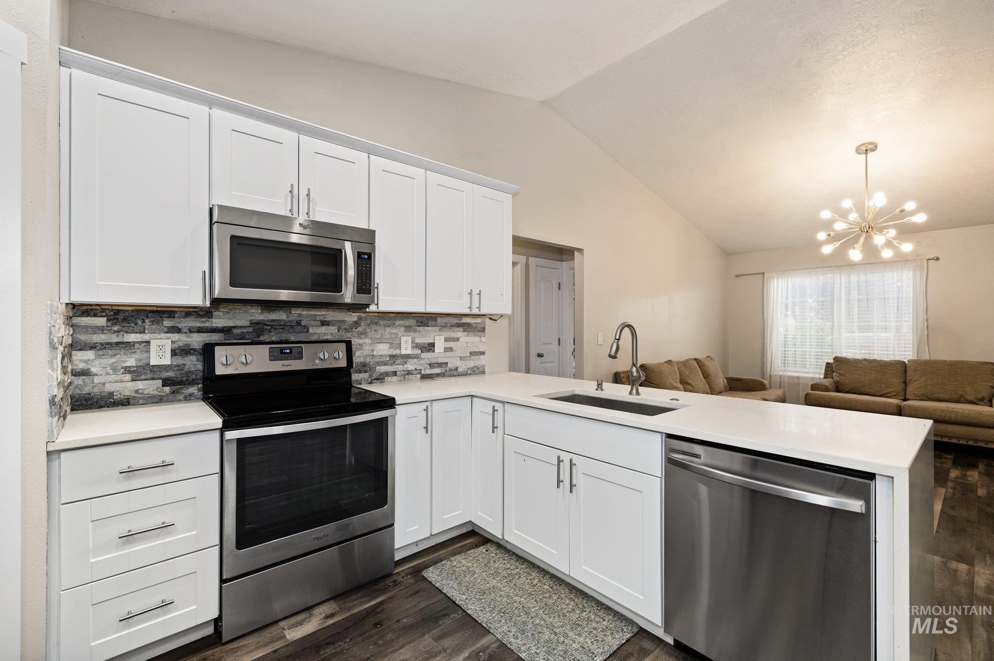 Kitchen with stainless steel appliances, white cabinetry, a chandelier, open floor plan, and dark wood-style flooring