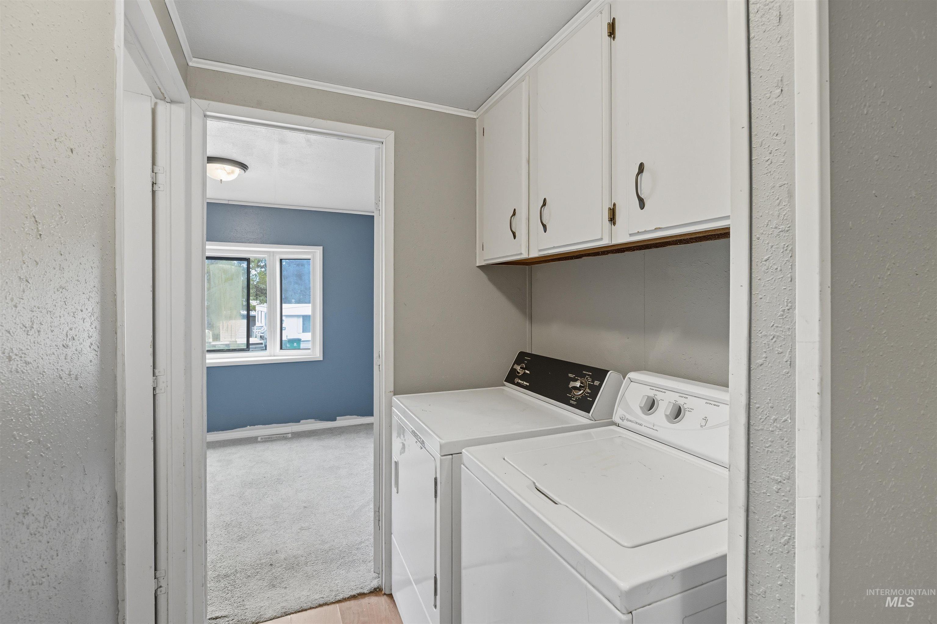 Laundry area with washing machine and clothes dryer, cabinet space, crown molding, light wood-type flooring, and light colored carpet