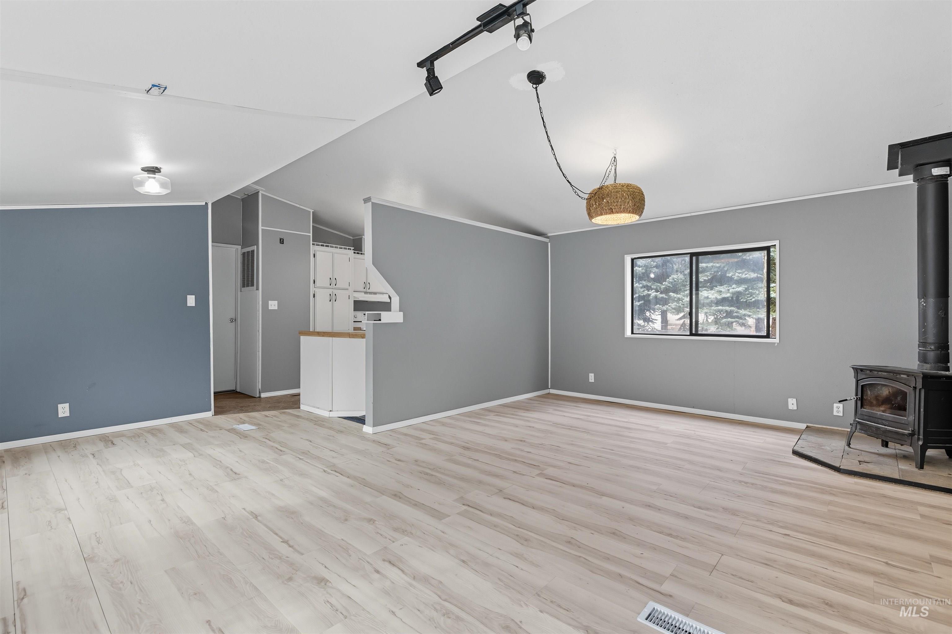 Unfurnished living room featuring a wood stove, light wood finished floors, and lofted ceiling