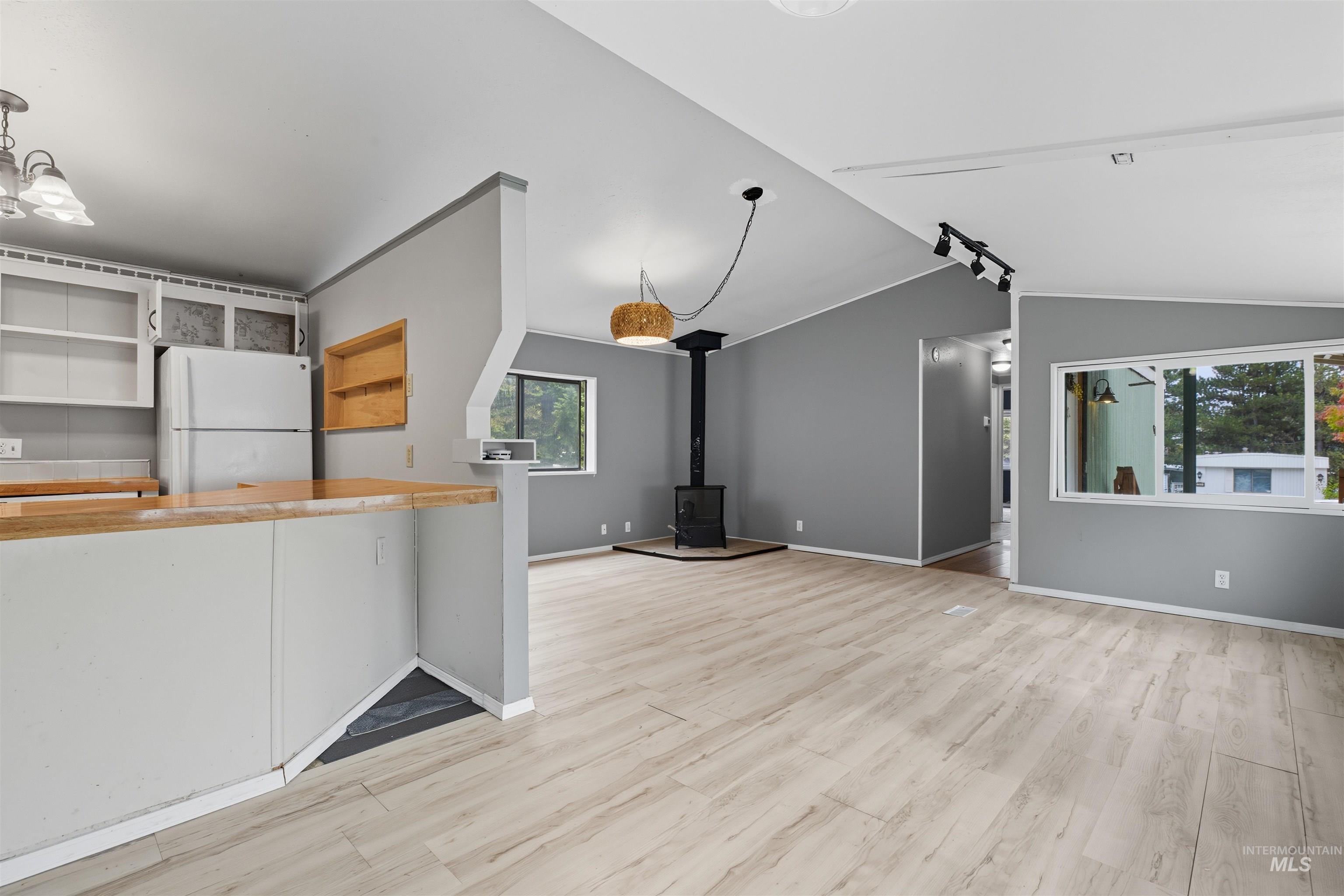 Unfurnished living room with a wood stove, light wood finished floors, and lofted ceiling