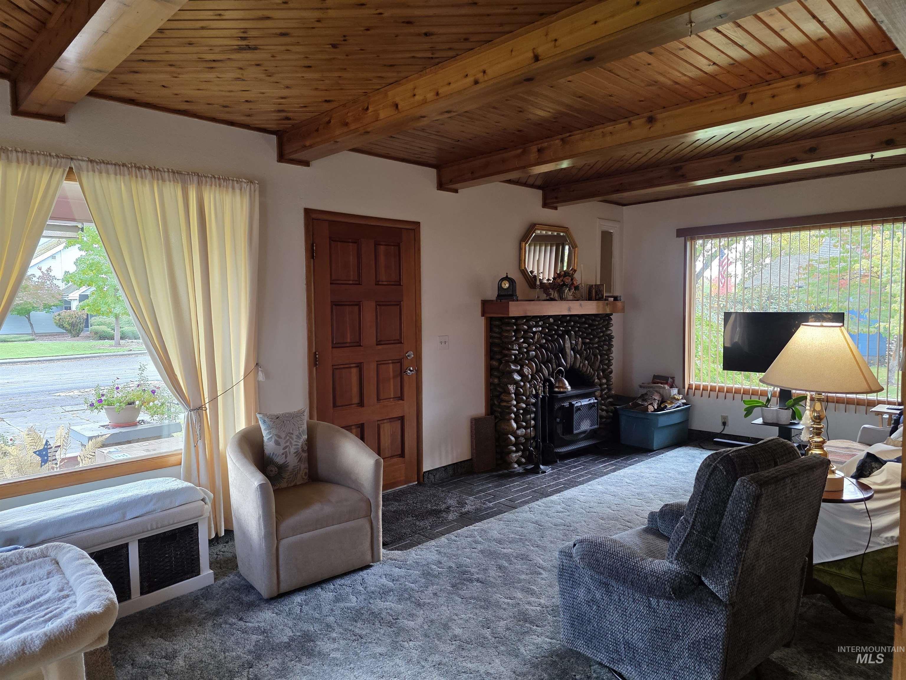 Living room with a wood stove and a wood ceiling with exposed beams