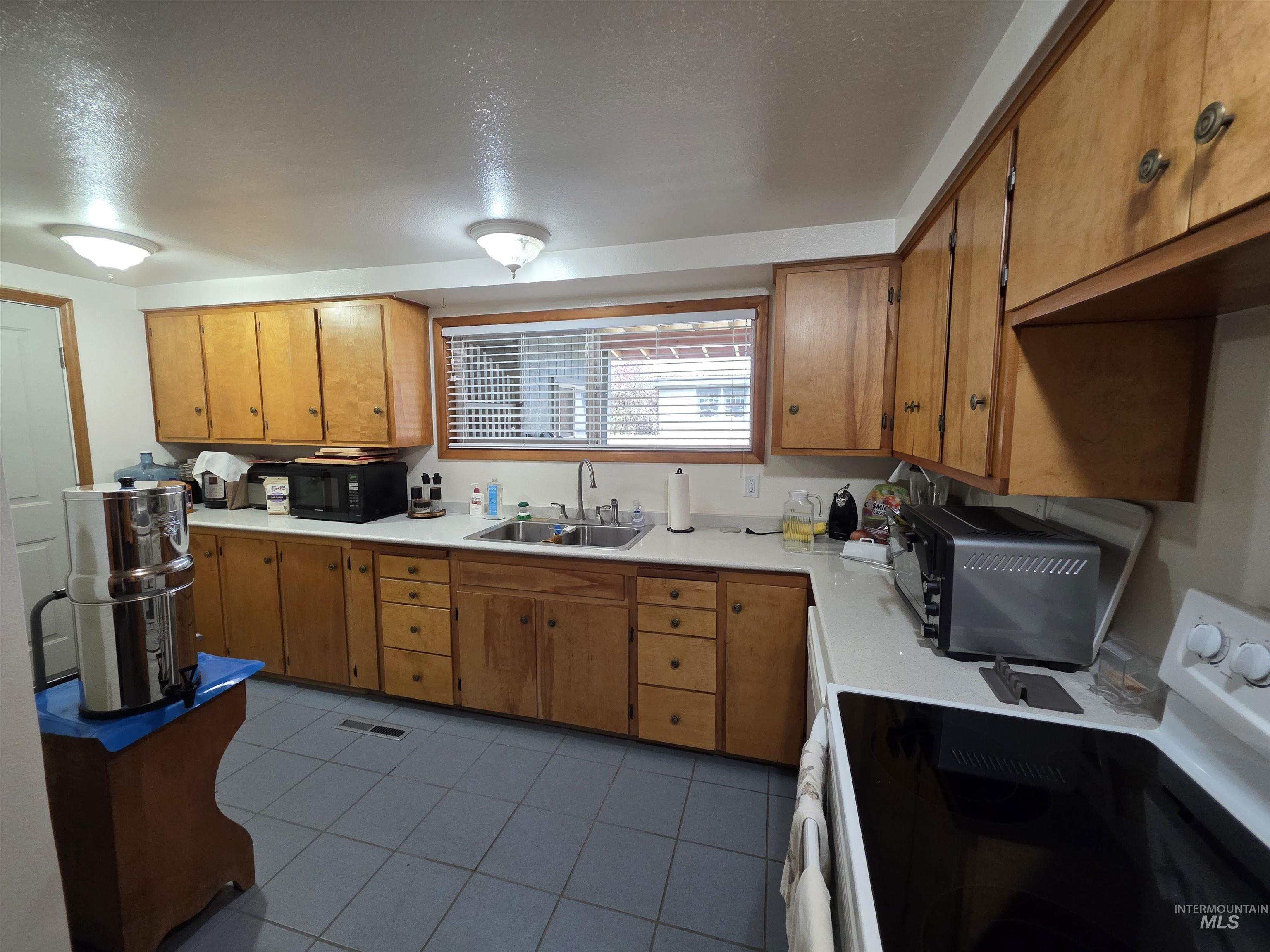 Kitchen with electric stove, light tile patterned floors, brown cabinetry, black microwave, and a textured ceiling