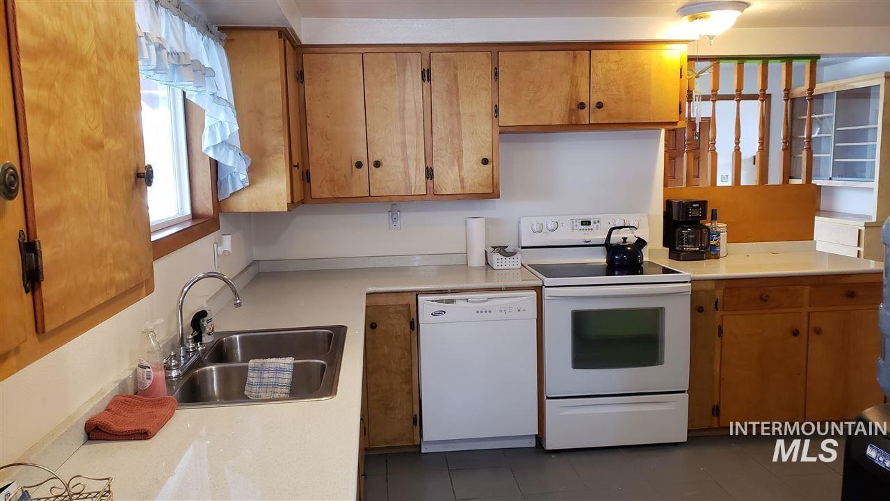 Kitchen featuring light countertops, white appliances, dark tile patterned flooring, and brown cabinetry
