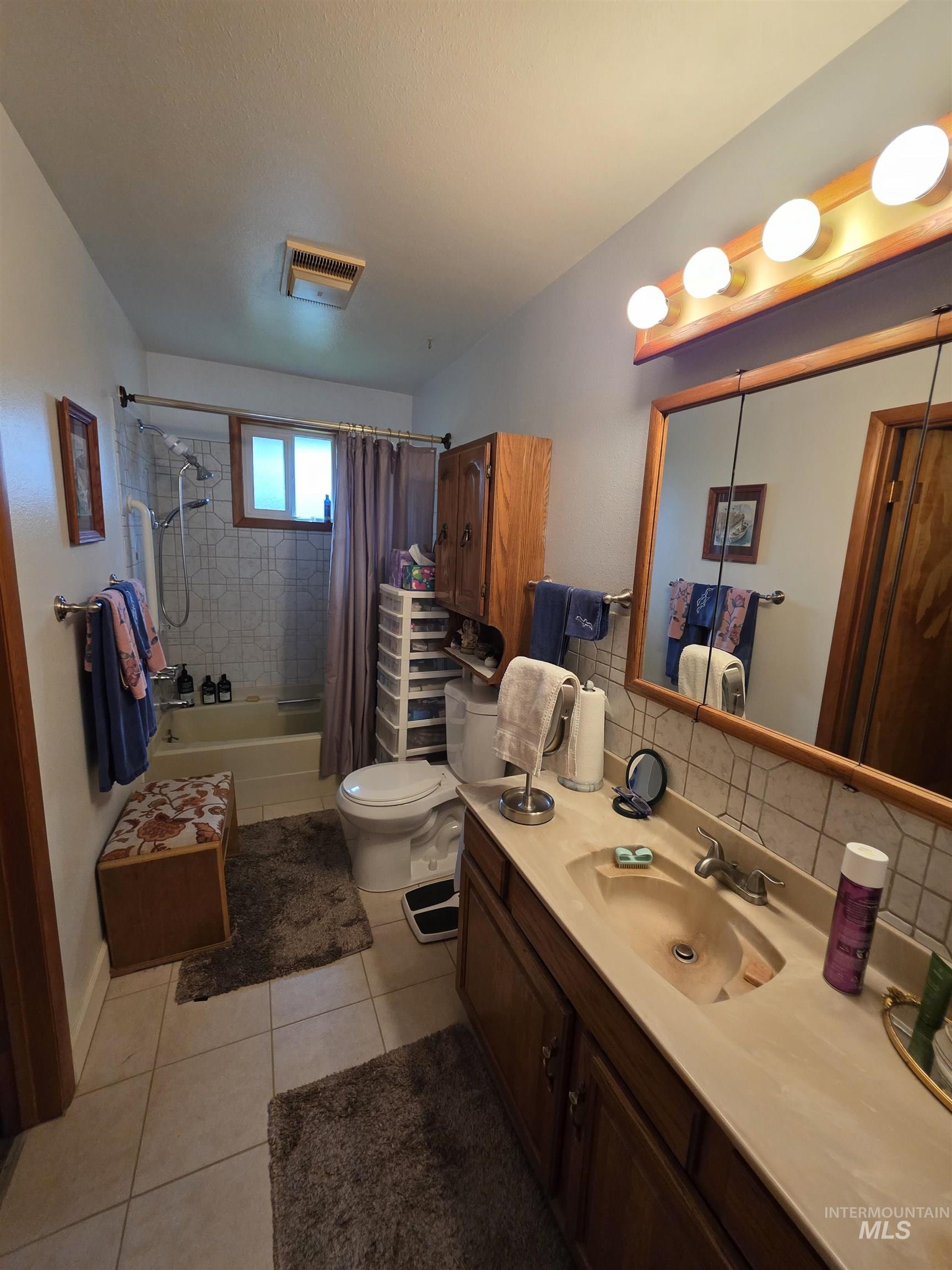 Bathroom featuring tiled shower / bath, vanity, light tile patterned floors, and decorative backsplash