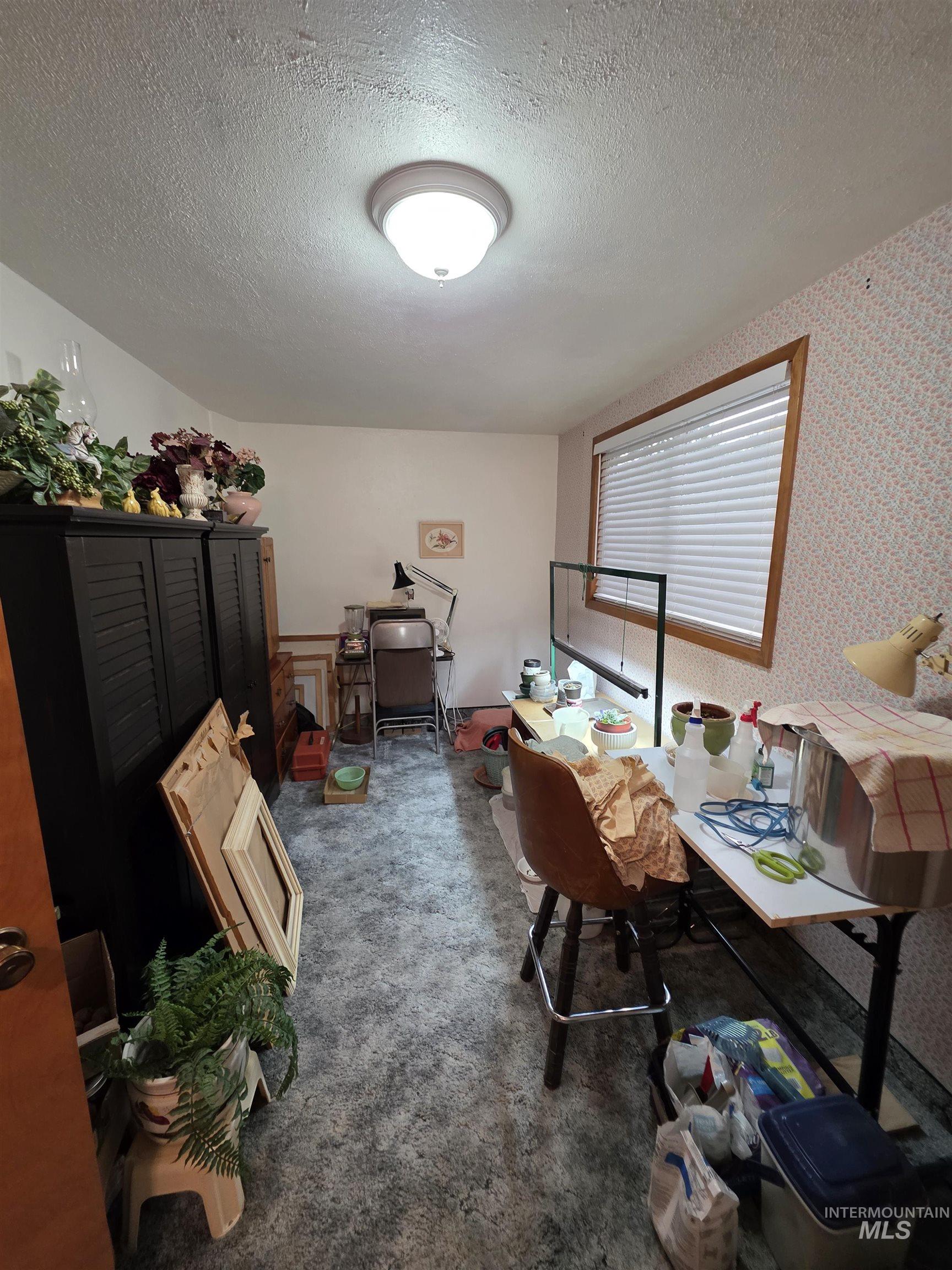 Office space with dark carpet, a textured ceiling, and wallpapered walls