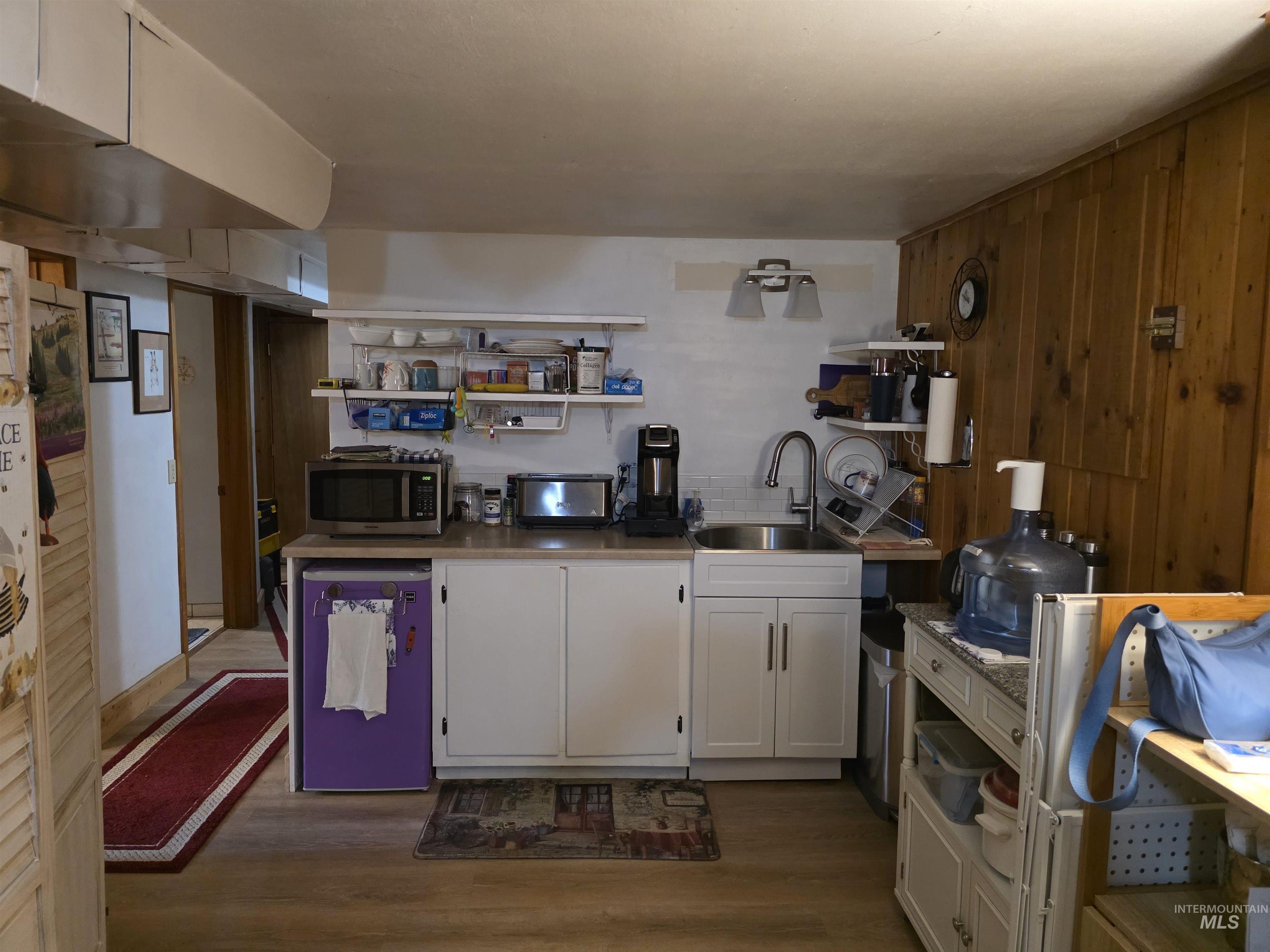Kitchen featuring open shelves, white cabinetry, dark wood-style flooring, stainless steel microwave, and light countertops
