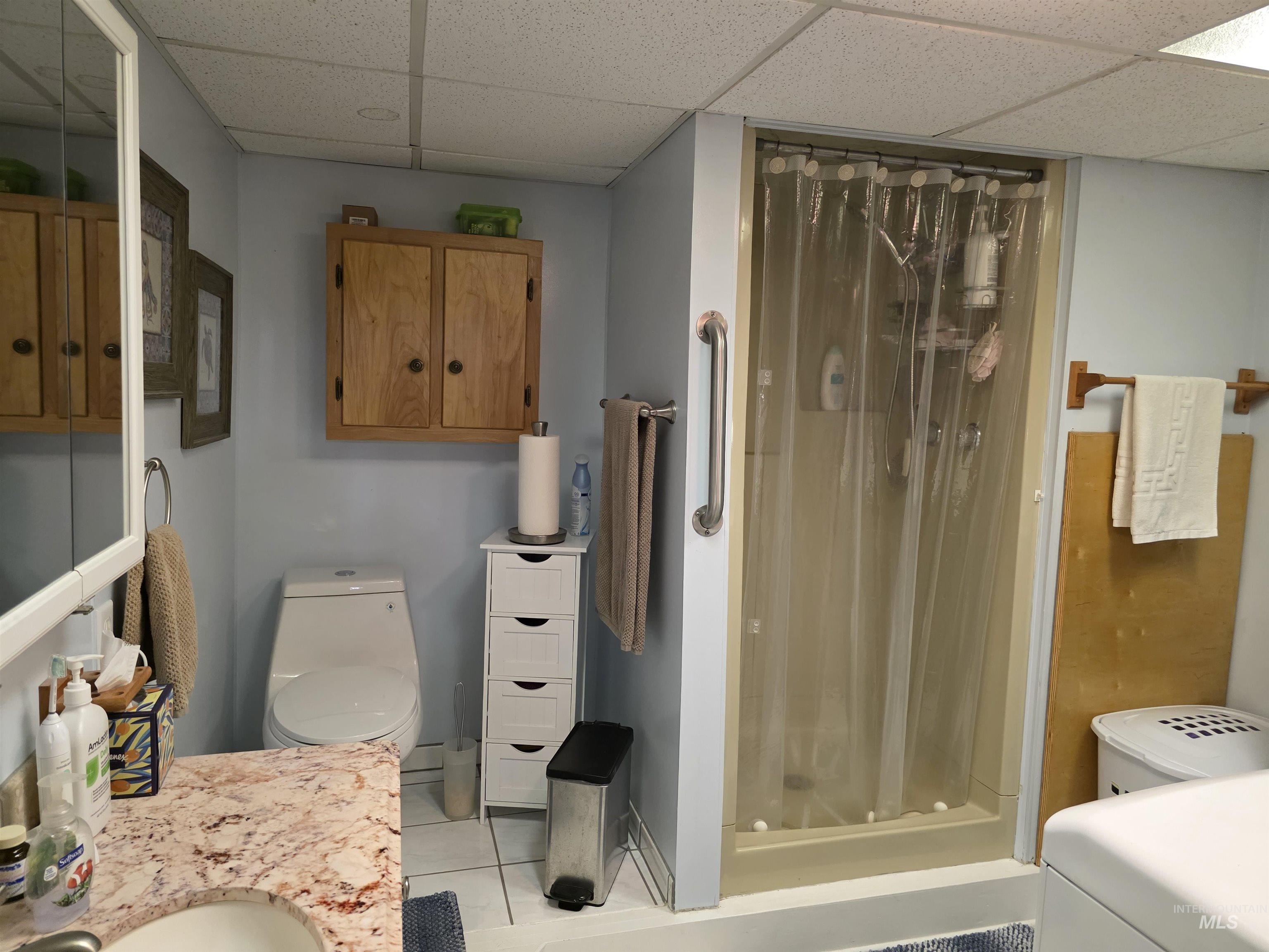 Bathroom with light tile patterned floors, a shower stall, a paneled ceiling, vanity, and washer / clothes dryer