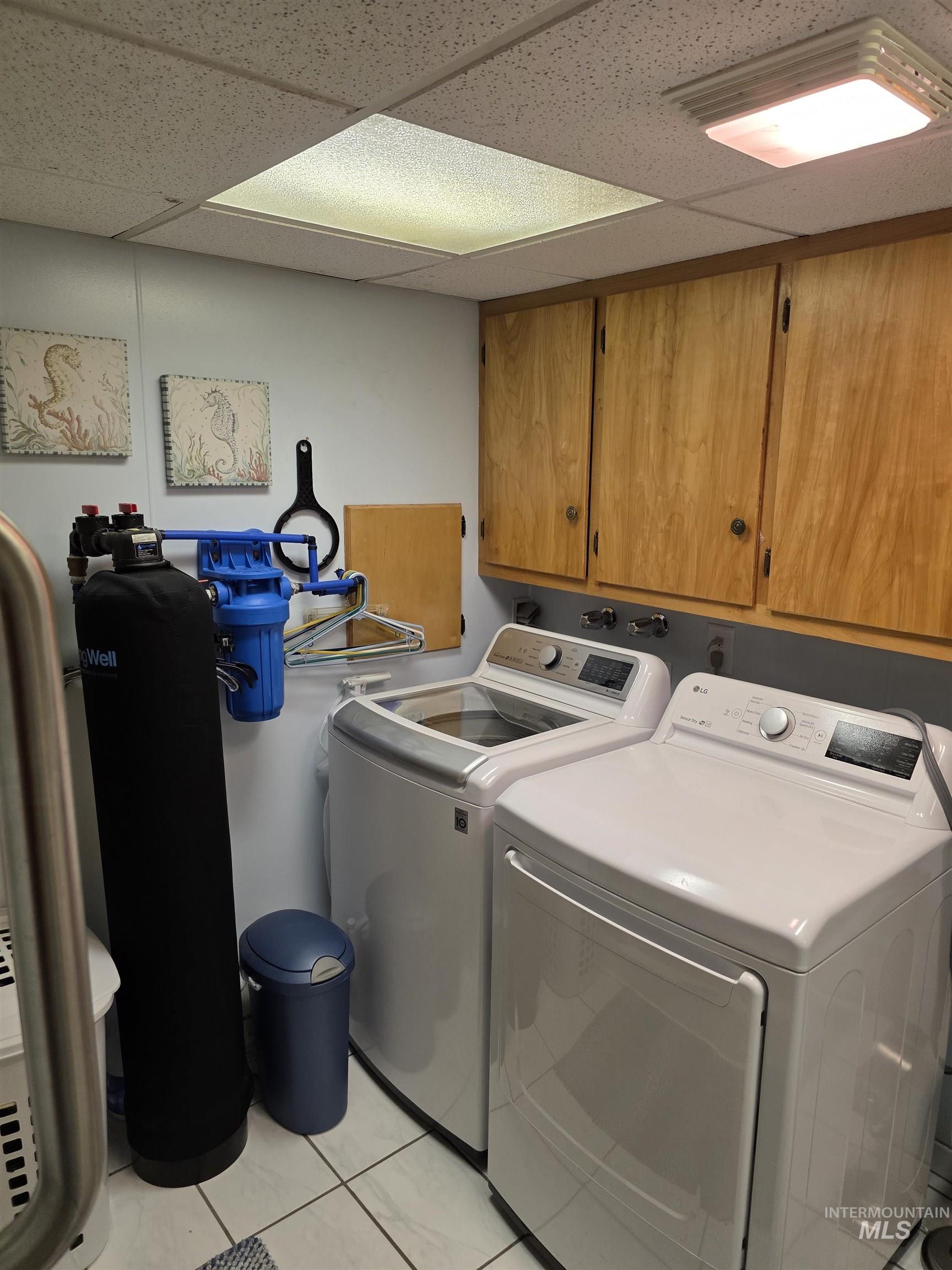 Washroom featuring separate washer and dryer, light tile patterned flooring, a drop ceiling, and cabinet space