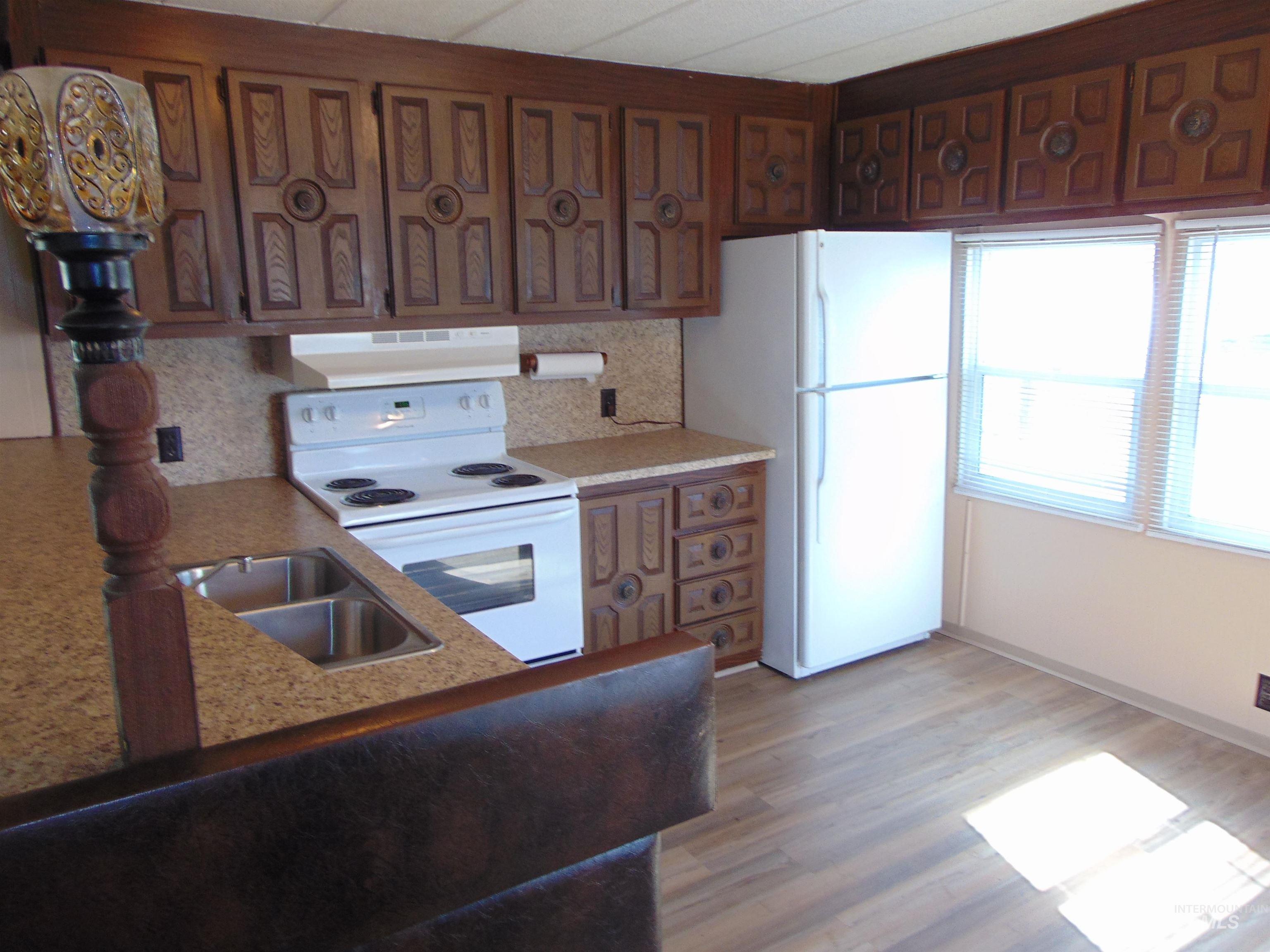 Kitchen with white appliances, light wood-style flooring, extractor fan, brown cabinetry, and backsplash