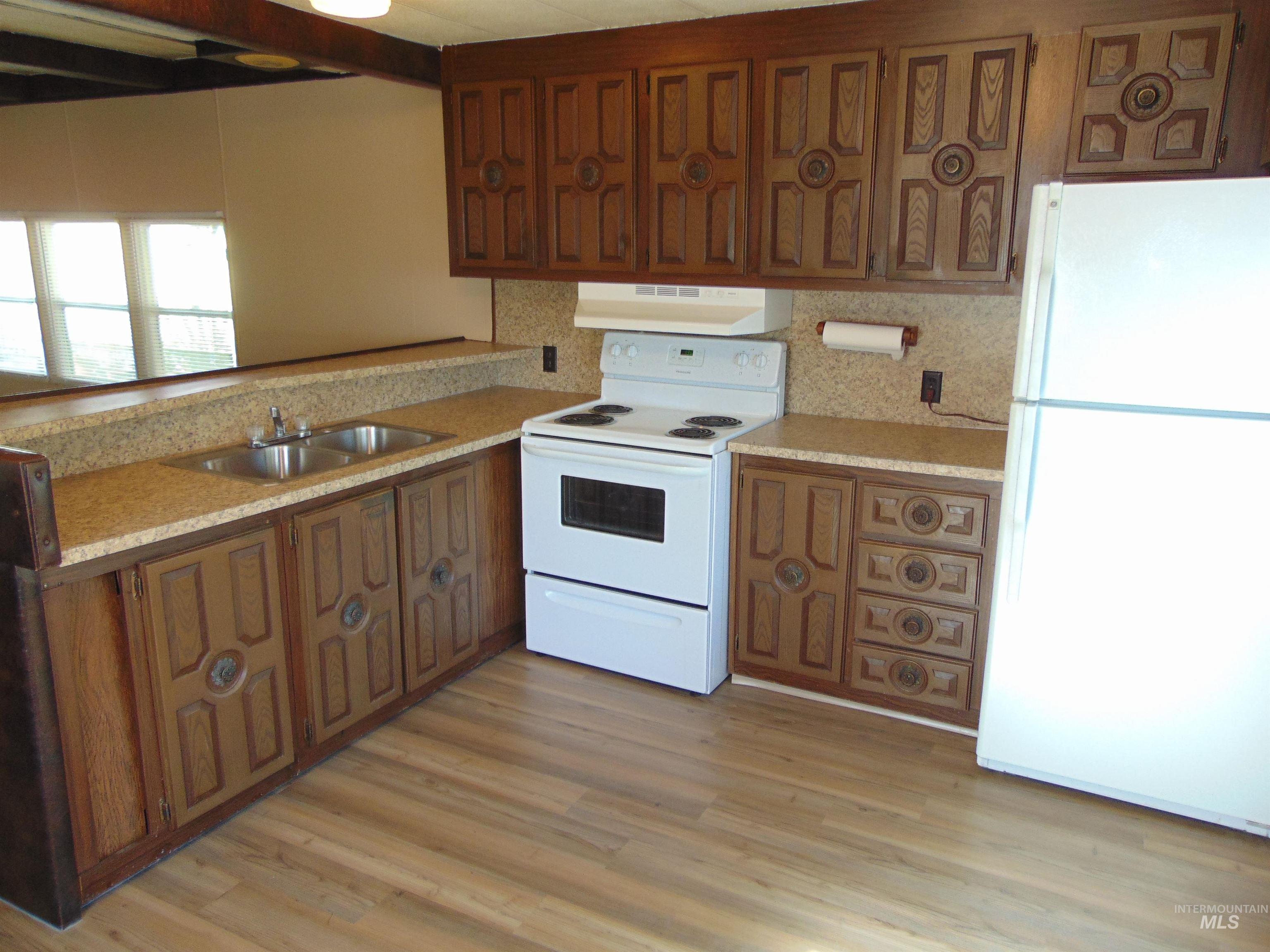 Kitchen featuring white appliances, under cabinet range hood, brown cabinetry, light wood finished floors, and light stone counters