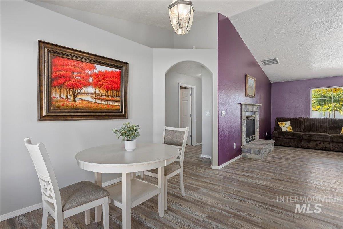 Dining area featuring arched walkways, a textured ceiling, wood finished floors, a stone fireplace, and lofted ceiling