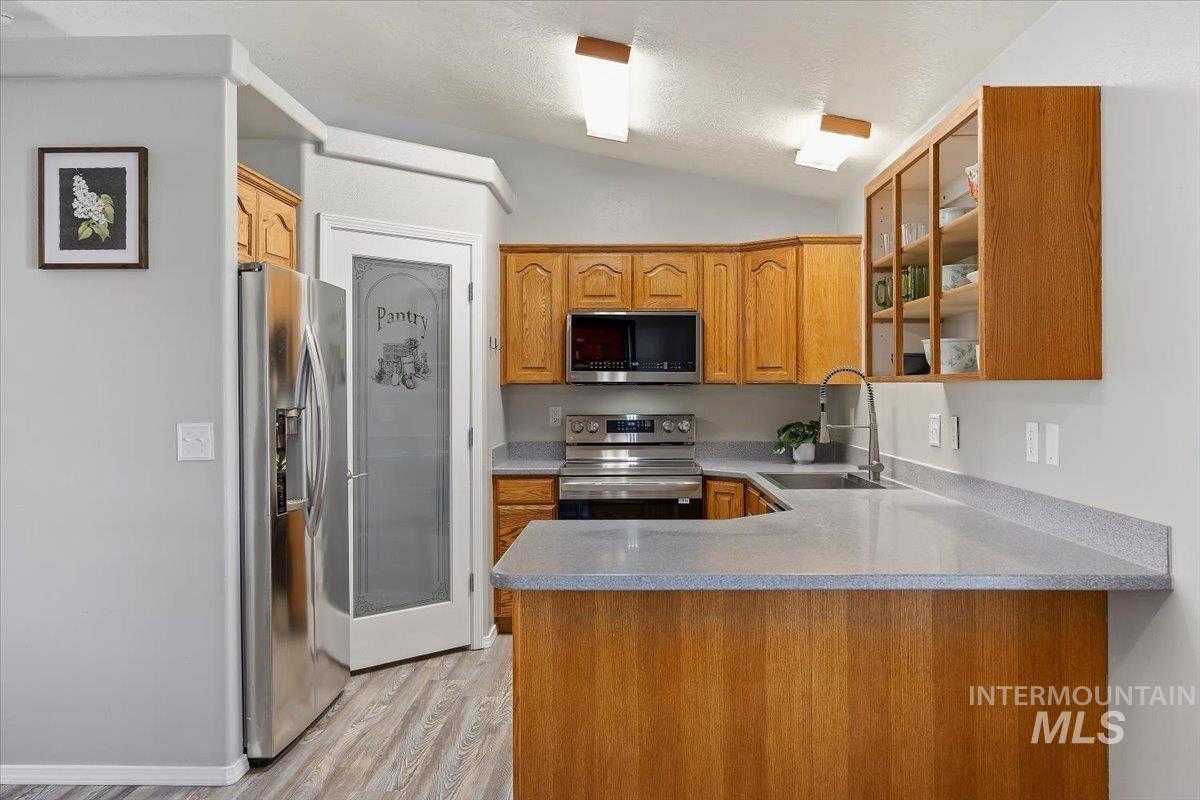 Kitchen with appliances with stainless steel finishes, a peninsula, light wood-type flooring, vaulted ceiling, and brown cabinetry