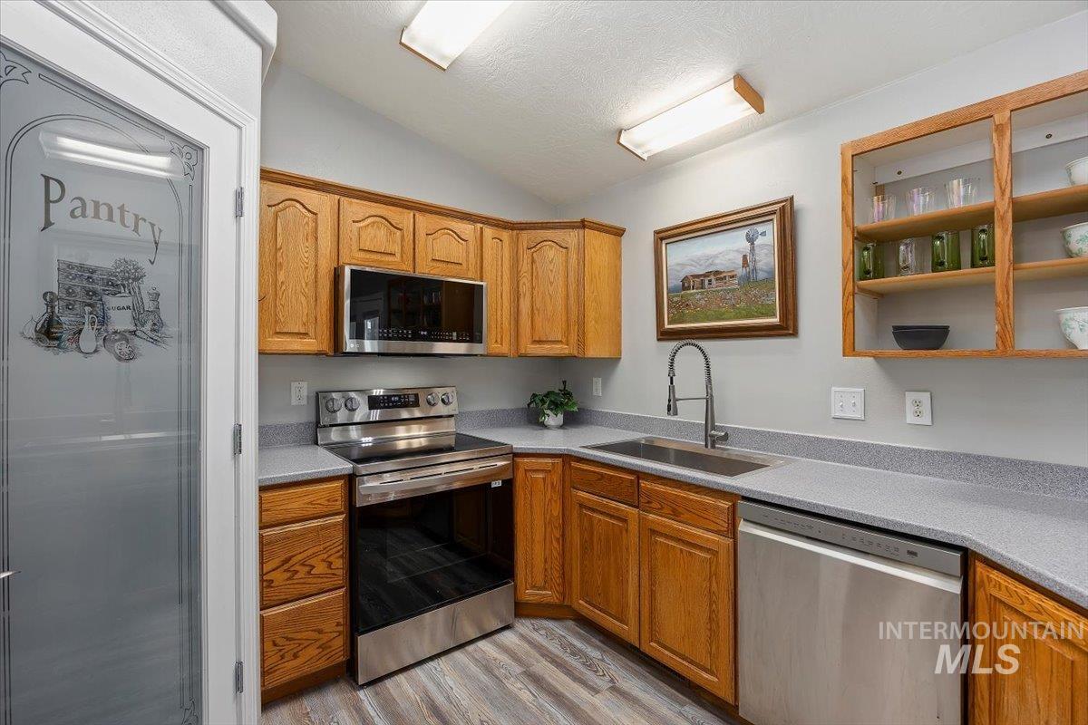 Kitchen with appliances with stainless steel finishes, lofted ceiling, light wood-type flooring, a textured ceiling, and light stone counters
