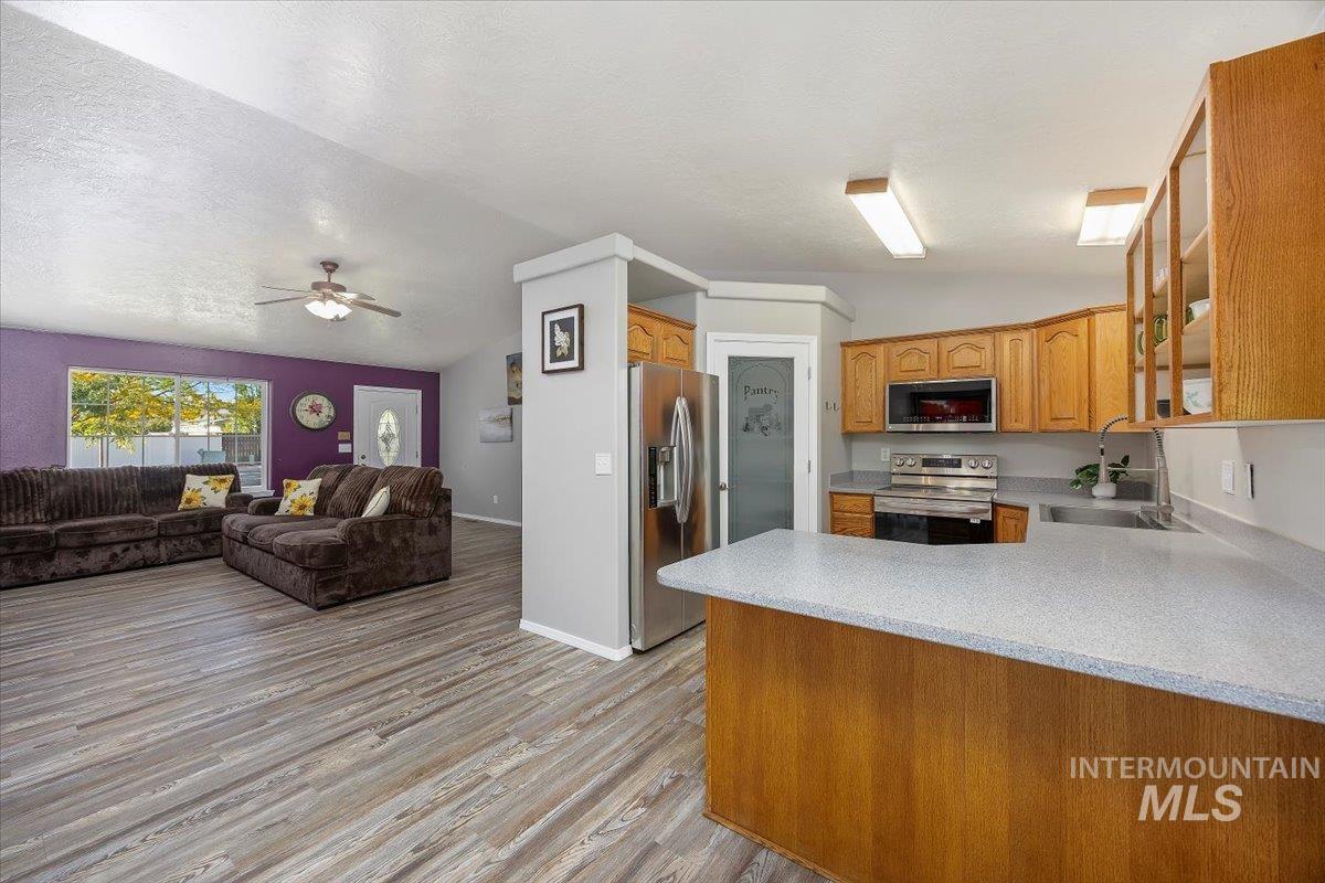 Kitchen featuring stainless steel appliances, glass insert cabinets, a peninsula, light wood-type flooring, and open floor plan