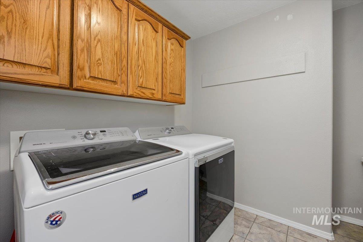 Washroom with cabinet space, washing machine and clothes dryer, and light tile patterned floors