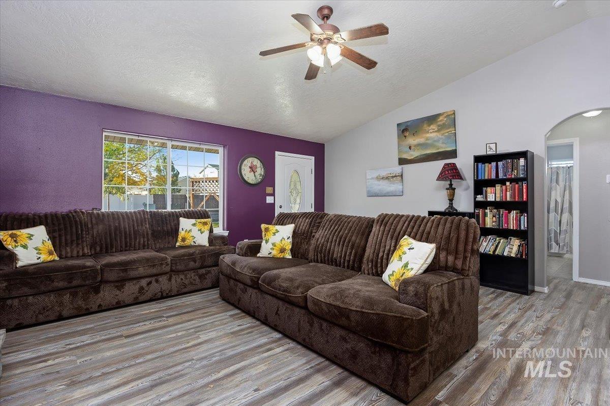 Living area featuring a textured ceiling, vaulted ceiling, ceiling fan, wood finished floors, and arched walkways