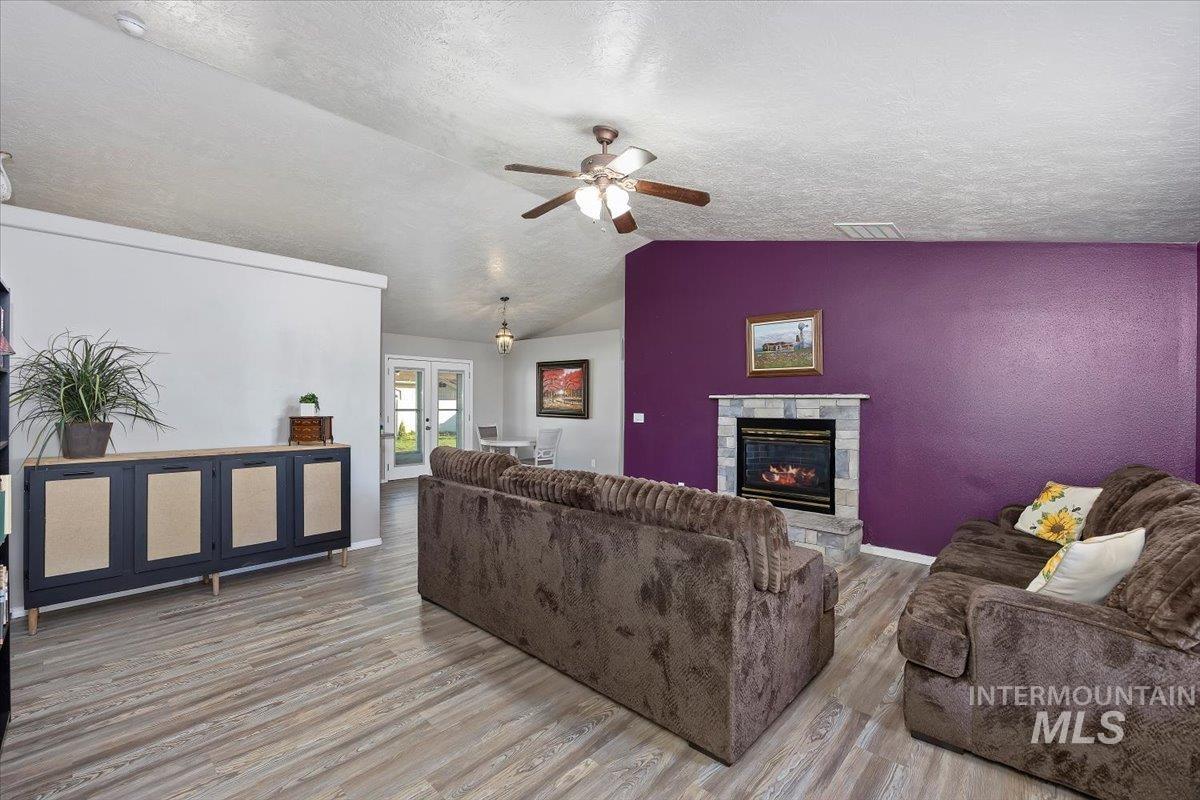Living area with french doors, vaulted ceiling, wood finished floors, a stone fireplace, and a textured ceiling