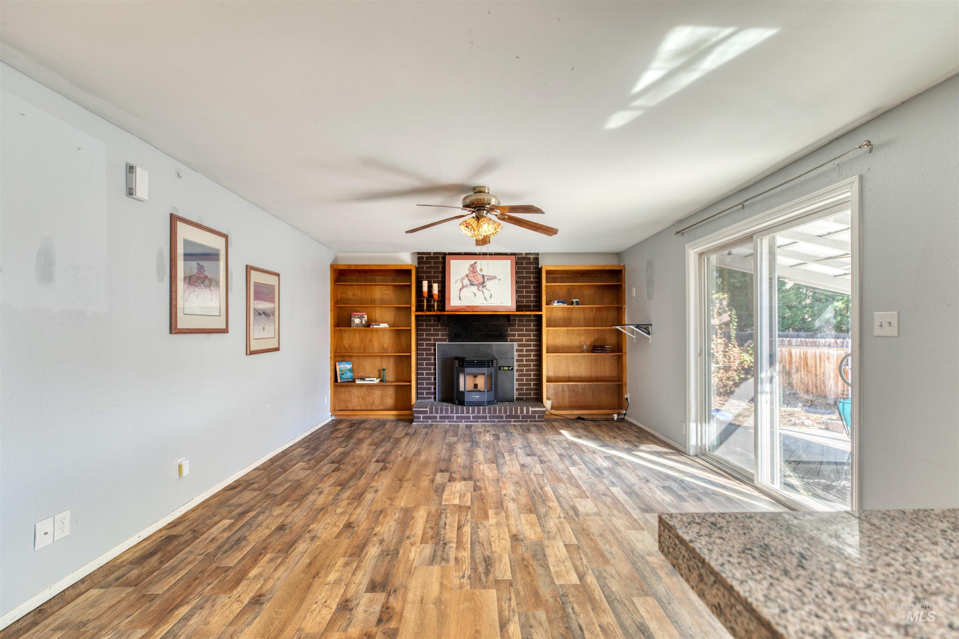 Unfurnished living room with wood finished floors, a ceiling fan, and built in shelves