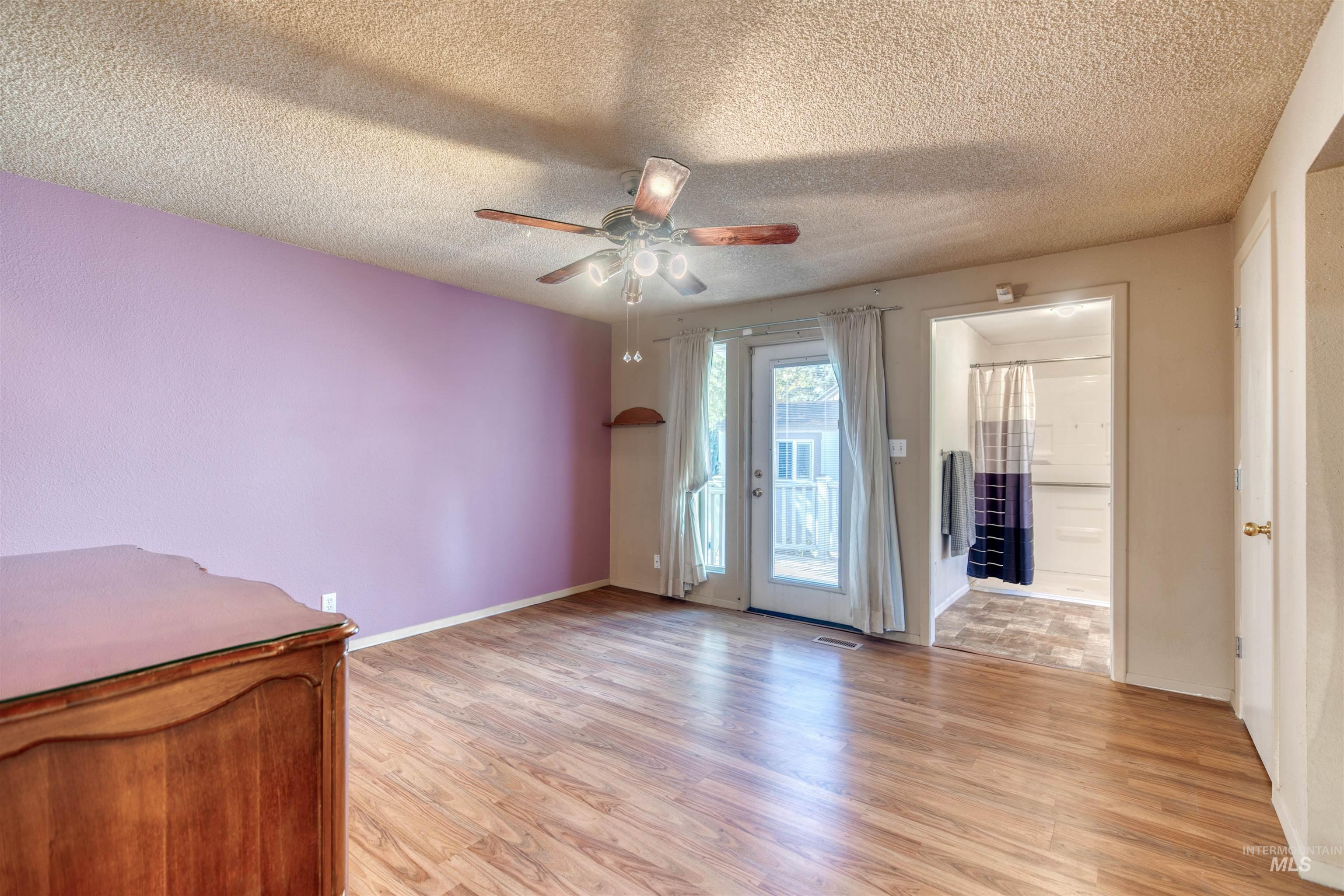 Empty room featuring light wood-style flooring, a textured ceiling, and a ceiling fan