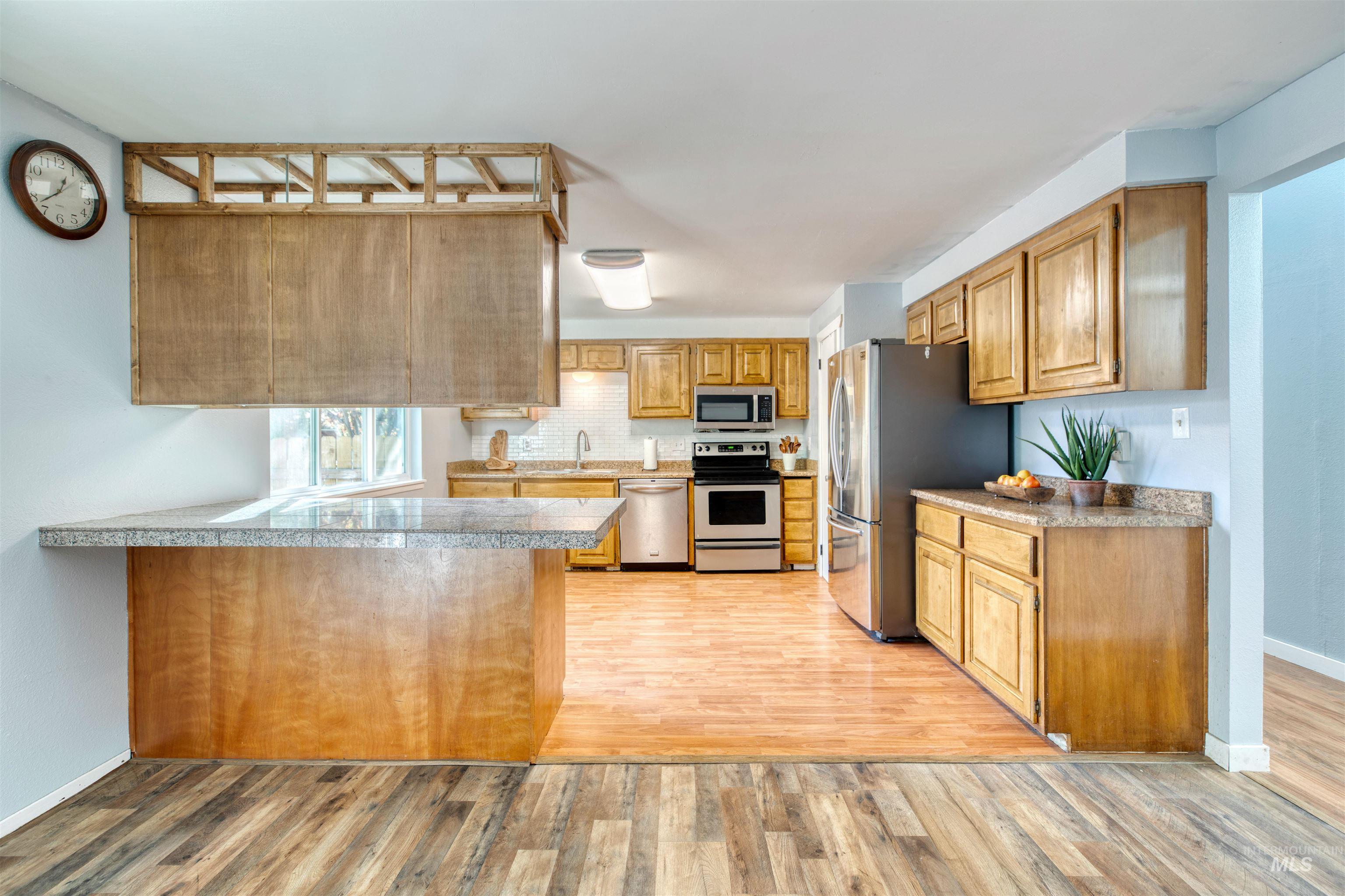 Kitchen featuring stainless steel appliances, light wood-type flooring, brown cabinets, backsplash, and a peninsula