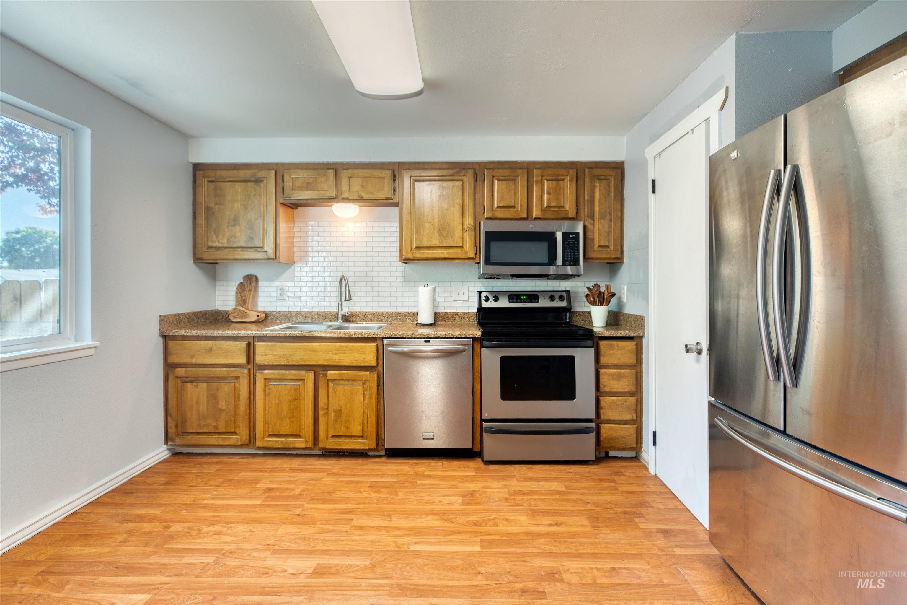 Kitchen featuring stainless steel appliances, brown cabinetry, light wood-style flooring, and backsplash