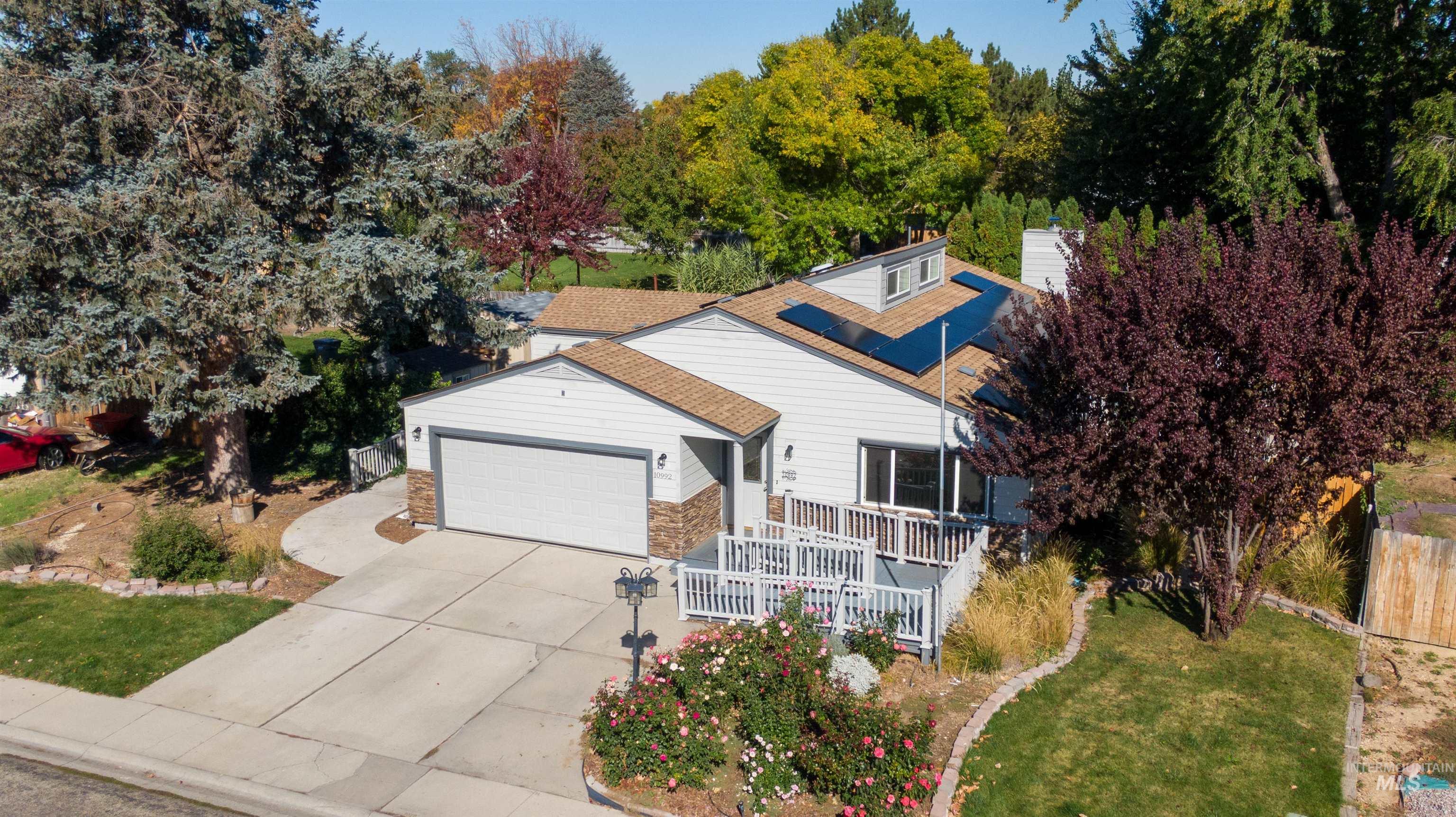 View of front of property with an attached garage, roof mounted solar panels, driveway, stone siding, and a deck