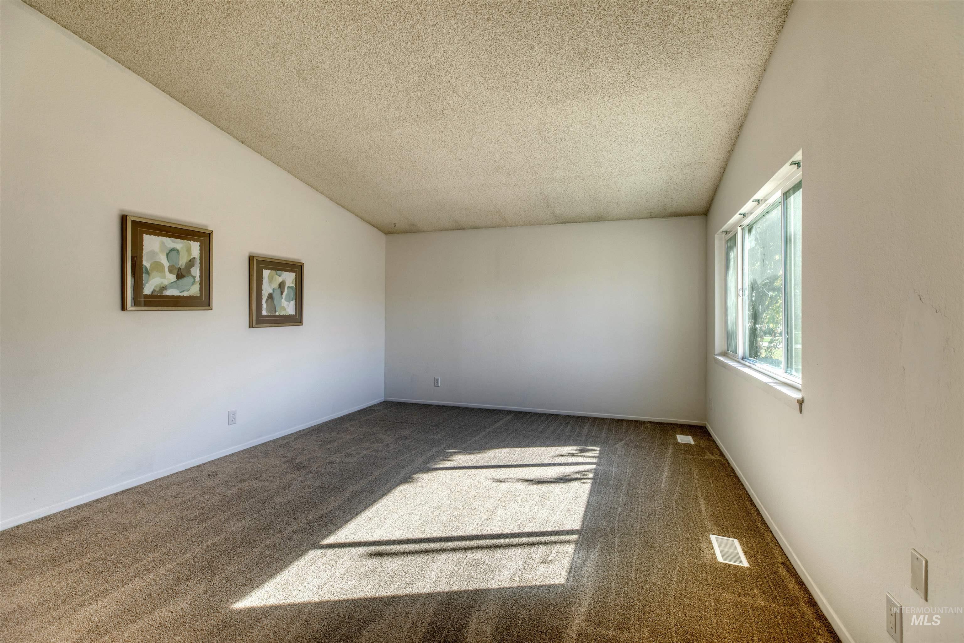 Carpeted spare room featuring vaulted ceiling and a textured ceiling