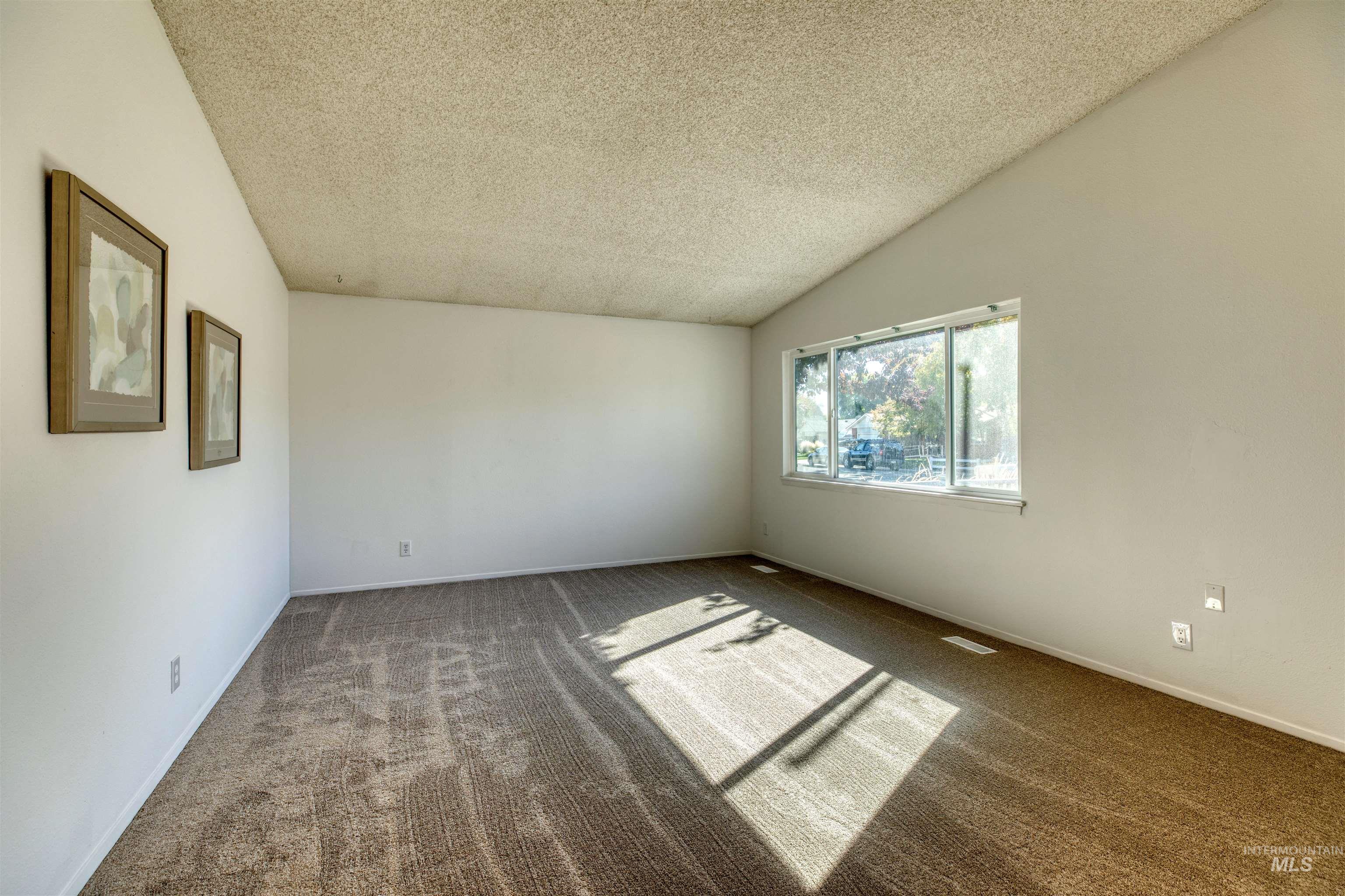 Carpeted empty room featuring lofted ceiling and a textured ceiling