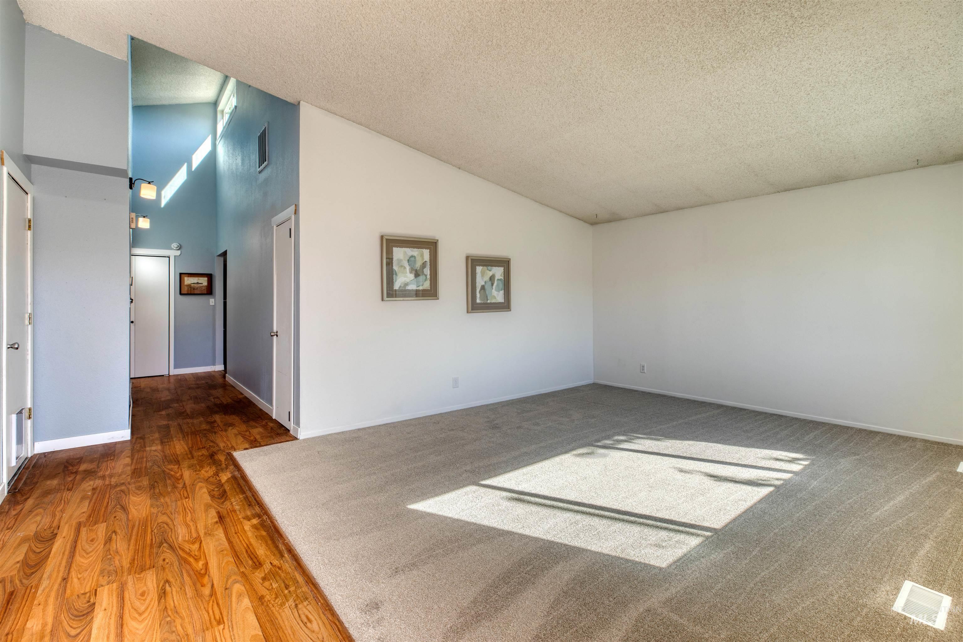 Empty room with a textured ceiling, wood finished floors, and high vaulted ceiling