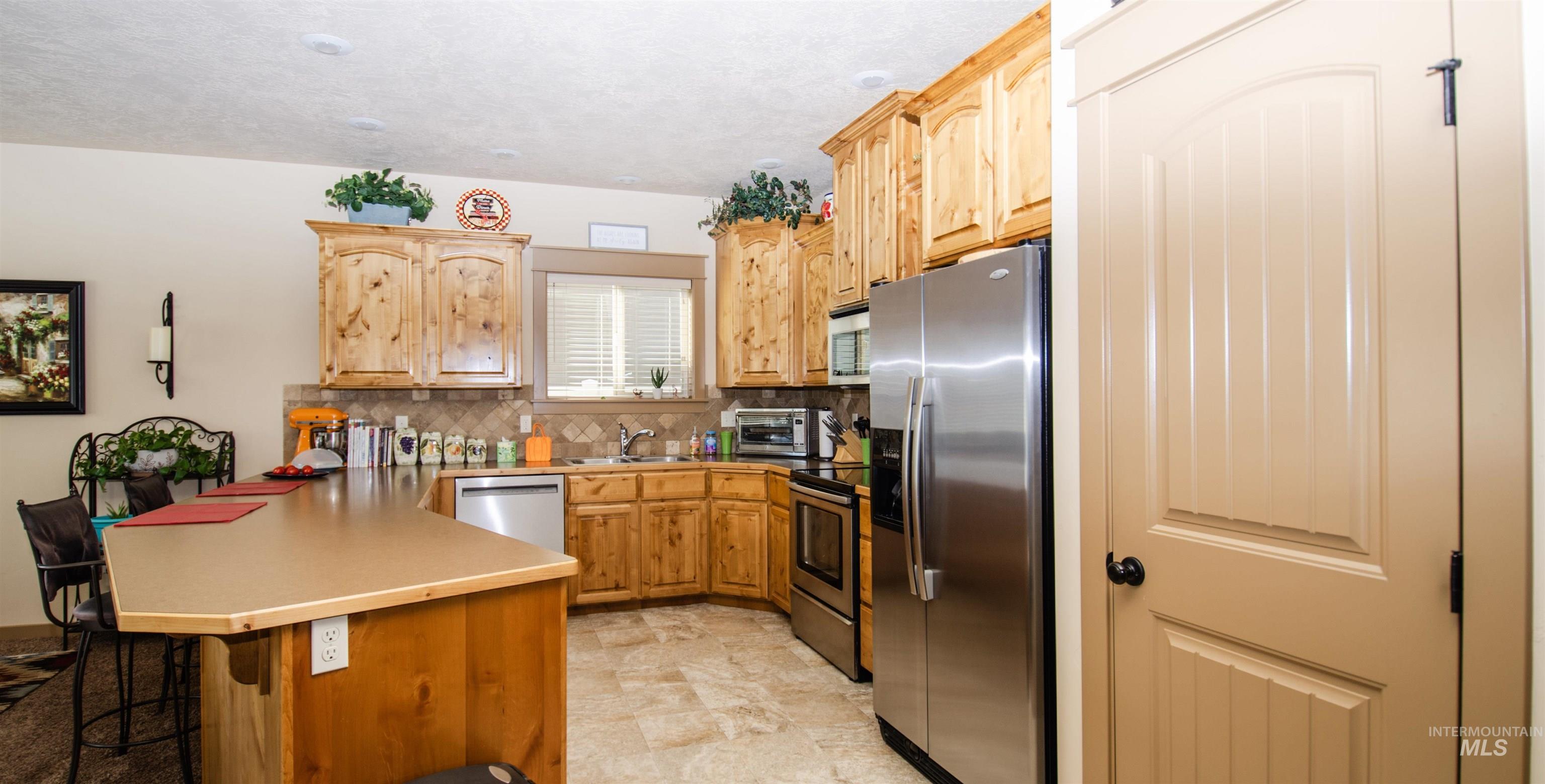 Kitchen featuring a peninsula, appliances with stainless steel finishes, a breakfast bar, decorative backsplash, and light countertops