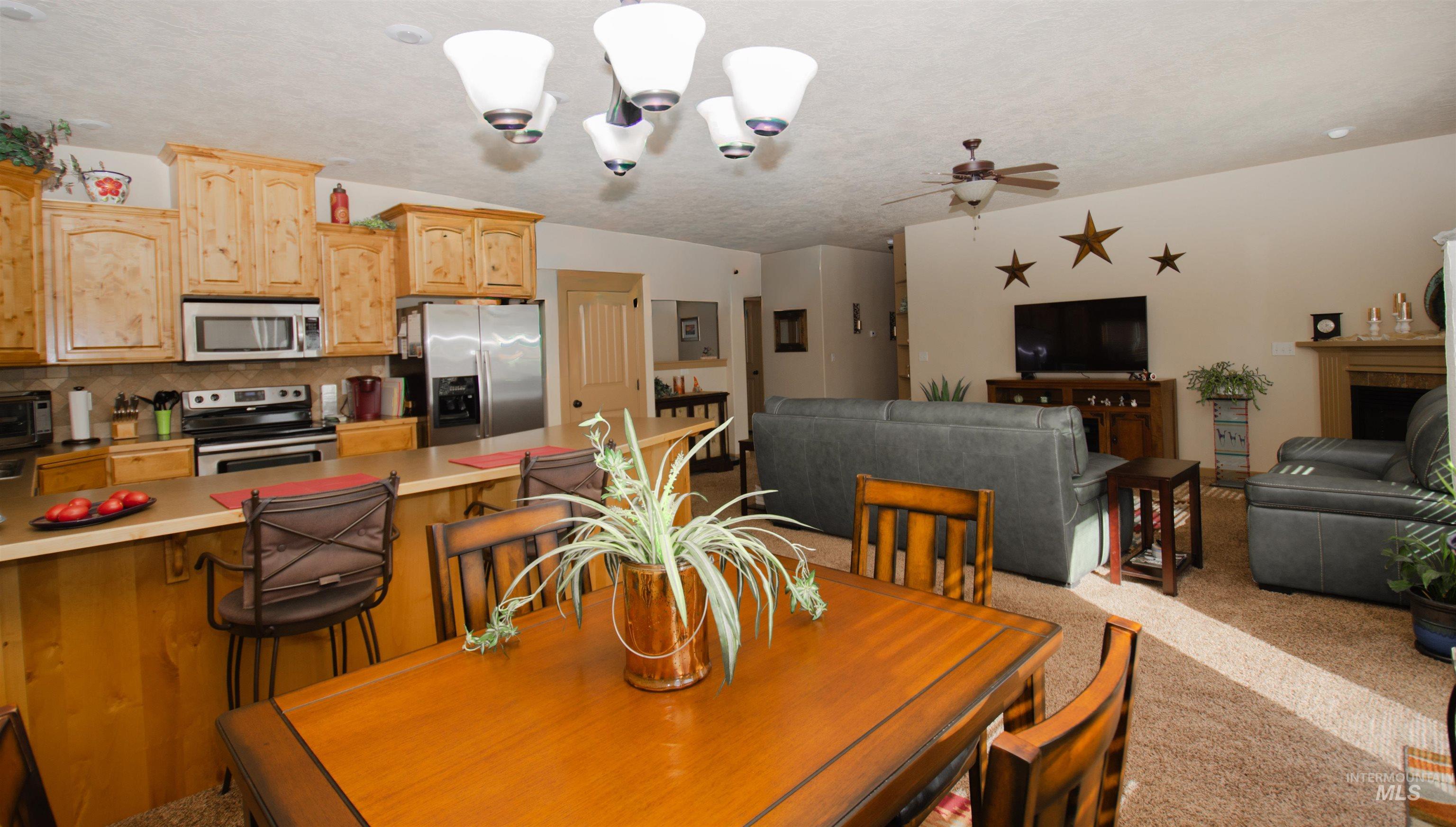 Dining room with a chandelier, light colored carpet, a fireplace, a ceiling fan, and a textured ceiling