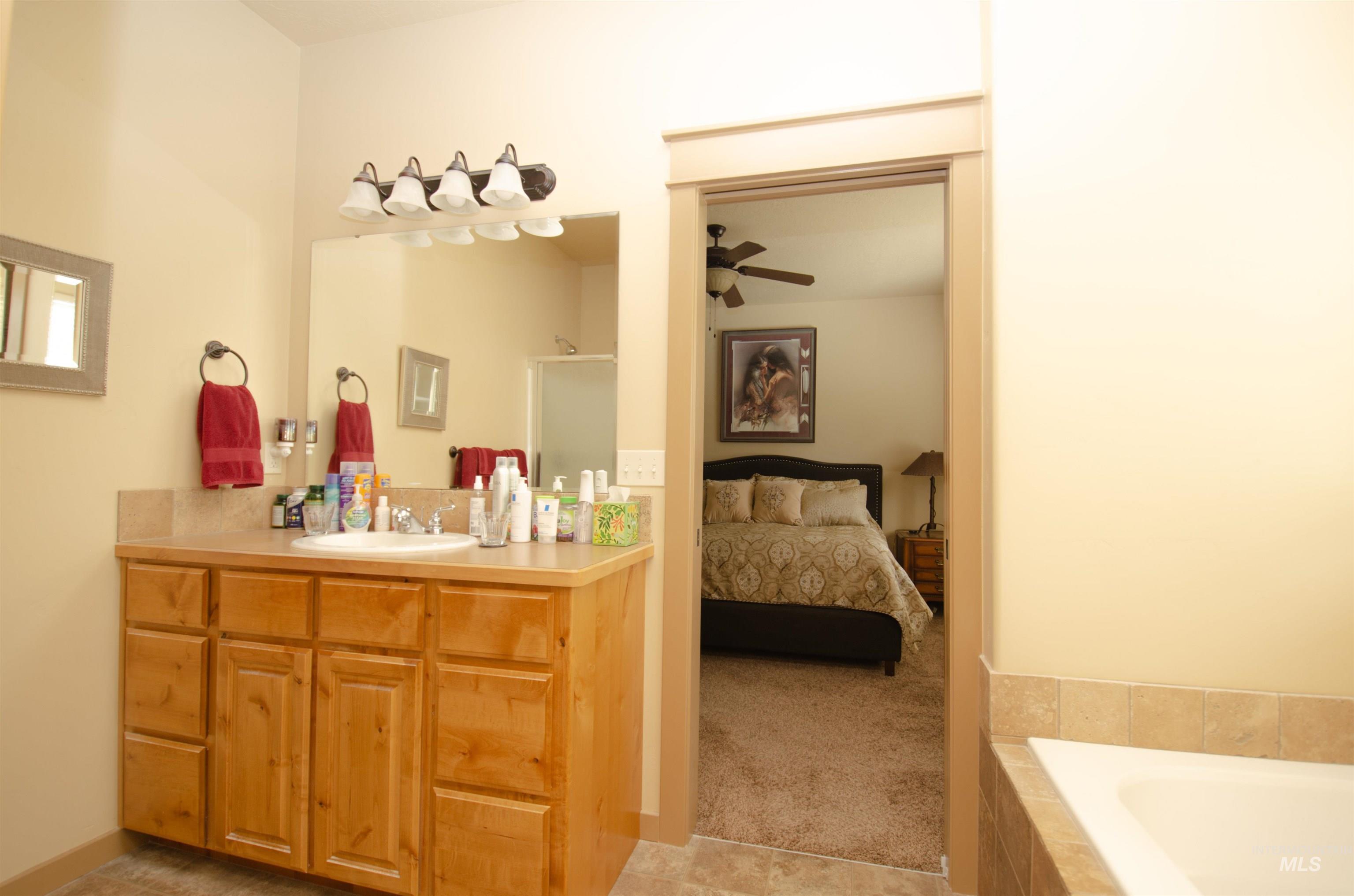 Ensuite bathroom with vanity, light tile patterned floors, tiled bath, and a ceiling fan