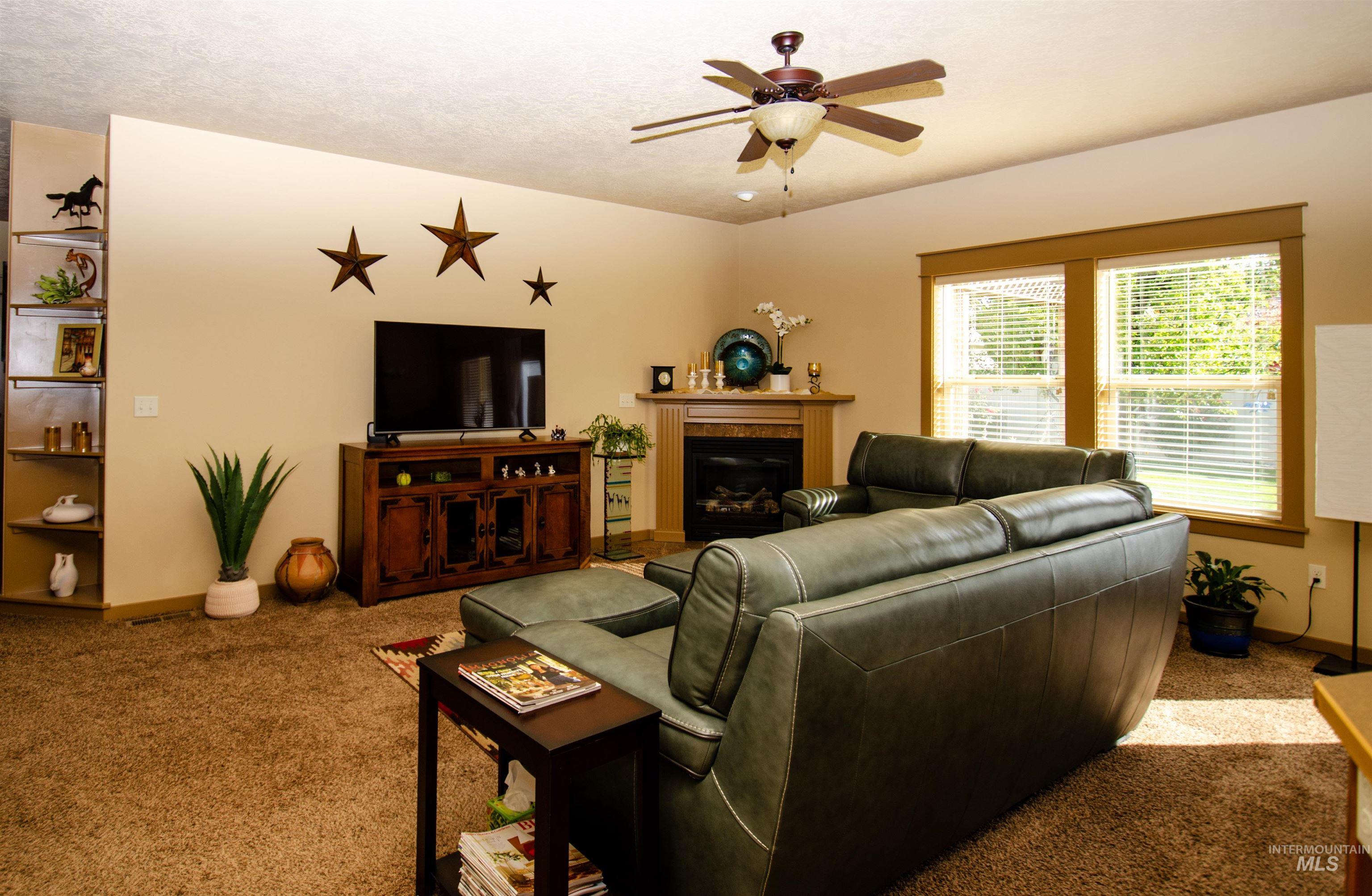 Carpeted living area featuring a glass covered fireplace and ceiling fan